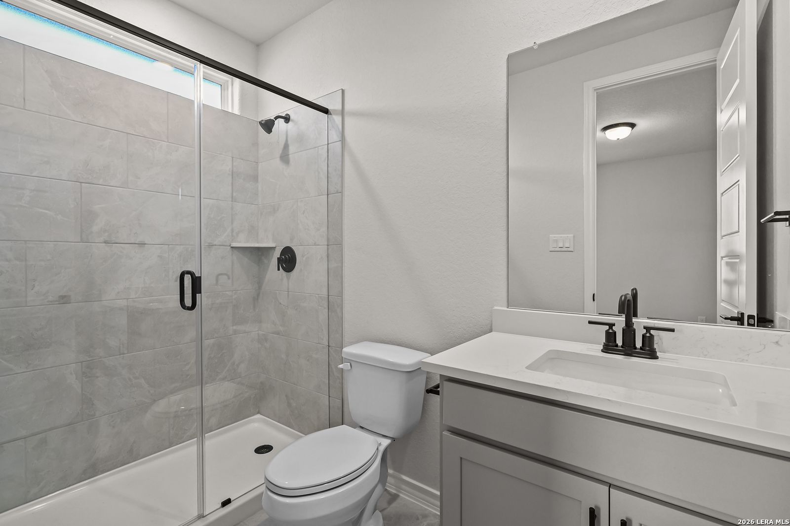 Modern bathroom with glass tile walk-in shower, quartz vanity, and matte black fixtures in Davidson Homes' The Oxford F, Castroville TX