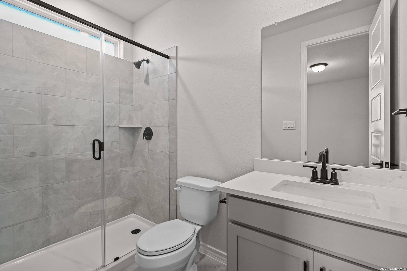 Modern bathroom with glass tile walk-in shower, quartz vanity, and matte black fixtures in Davidson Homes' The Oxford F, Castroville TX