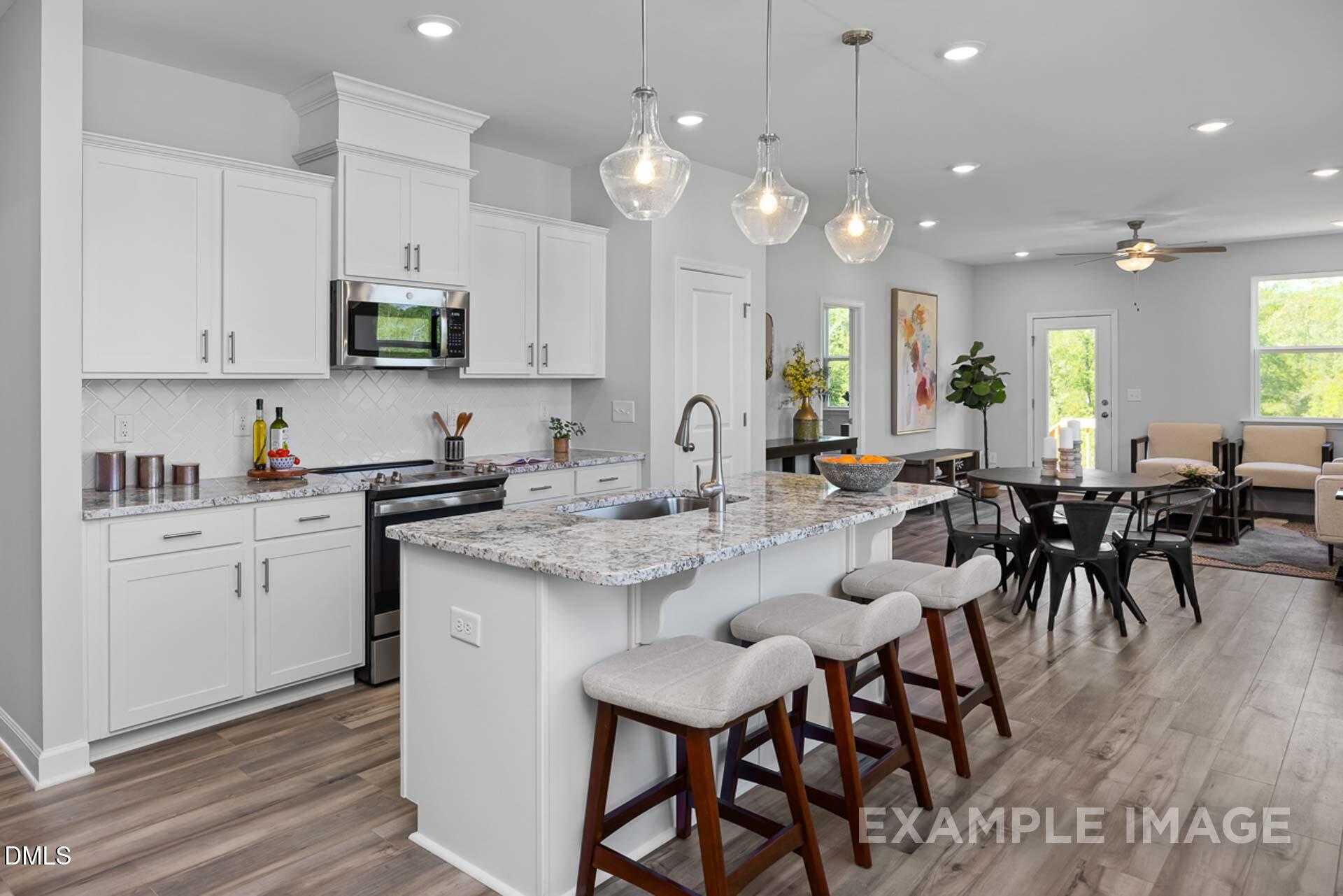 Modern open-concept kitchen with white cabinets, granite island, stainless appliances, and dining area in The Carter C, Lillington, NC