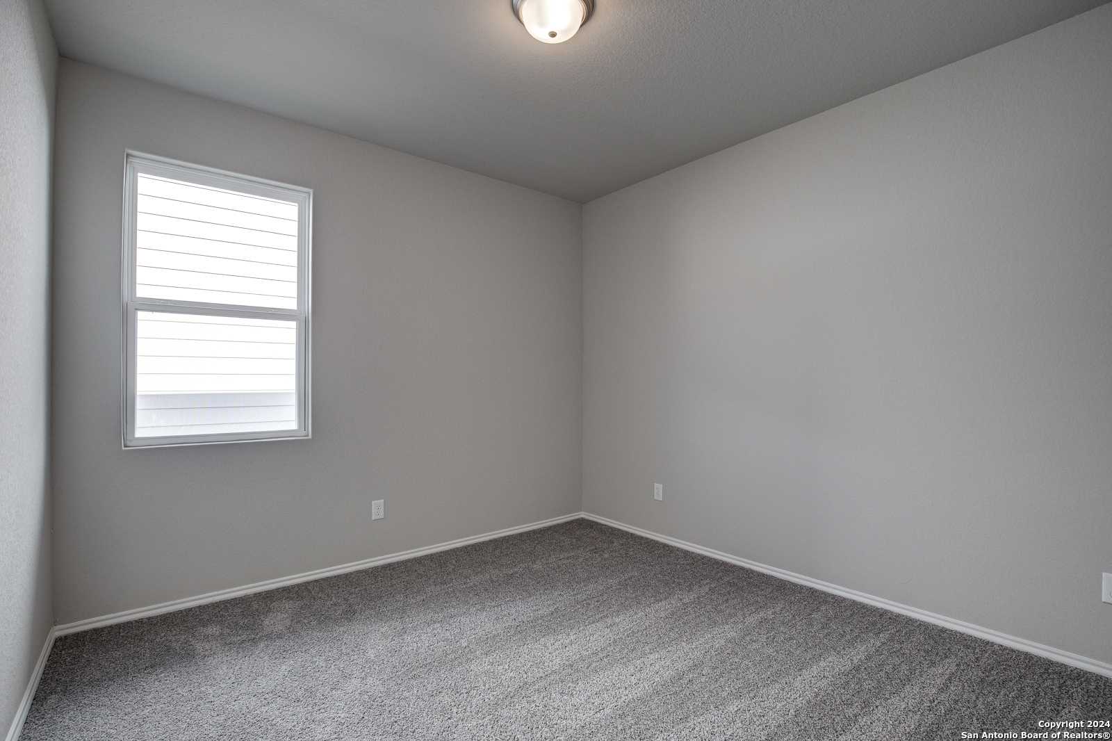 Cozy empty bedroom with gray carpet, walls, window blinds, and ceiling light in Davidson Homes The Frio B, San Antonio