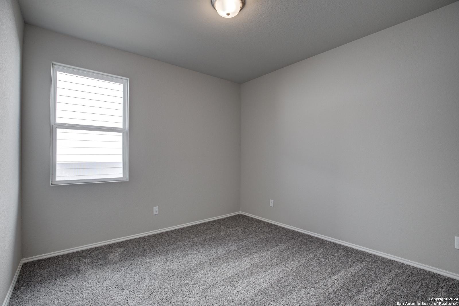 Cozy empty bedroom with gray carpet, walls, window blinds, and ceiling light in Davidson Homes The Frio B, San Antonio