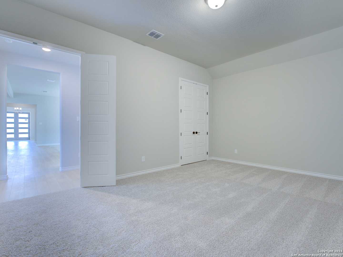 Spacious empty bedroom with open closet doors and foyer view in Davidson Homes The Summerlin A, Castroville Texas