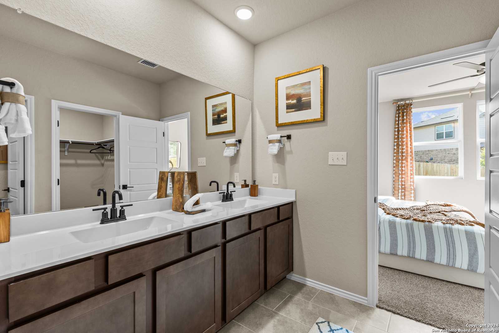 Elegant master bathroom featuring double wood vanity, mirrors, towels, and door to bedroom in Davidson Homes The Douglas F, Bricewood, San Antonio
