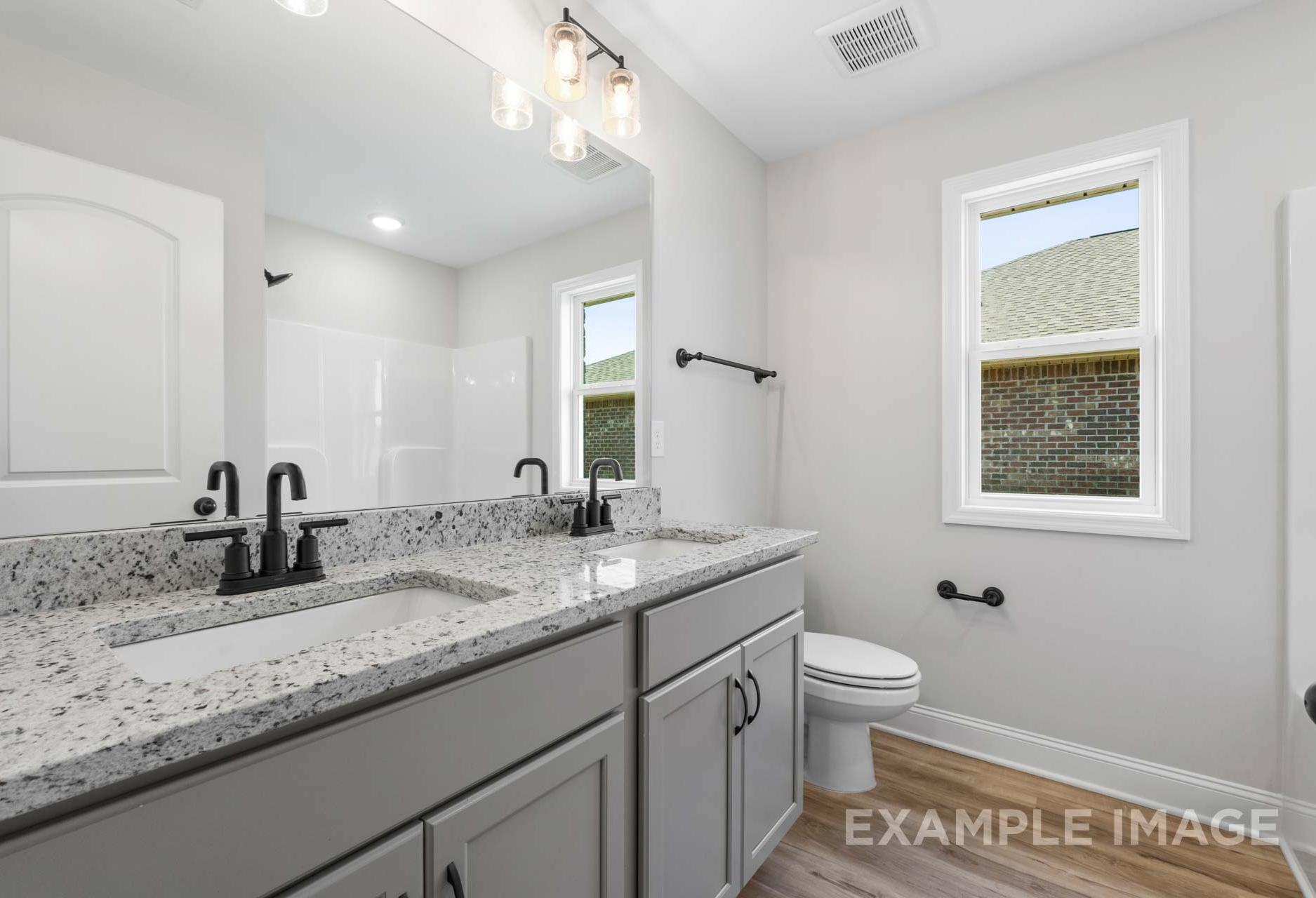 Modern master bathroom in The Holly M featuring double gray vanity, quartz counters, black faucets, and pendant lights