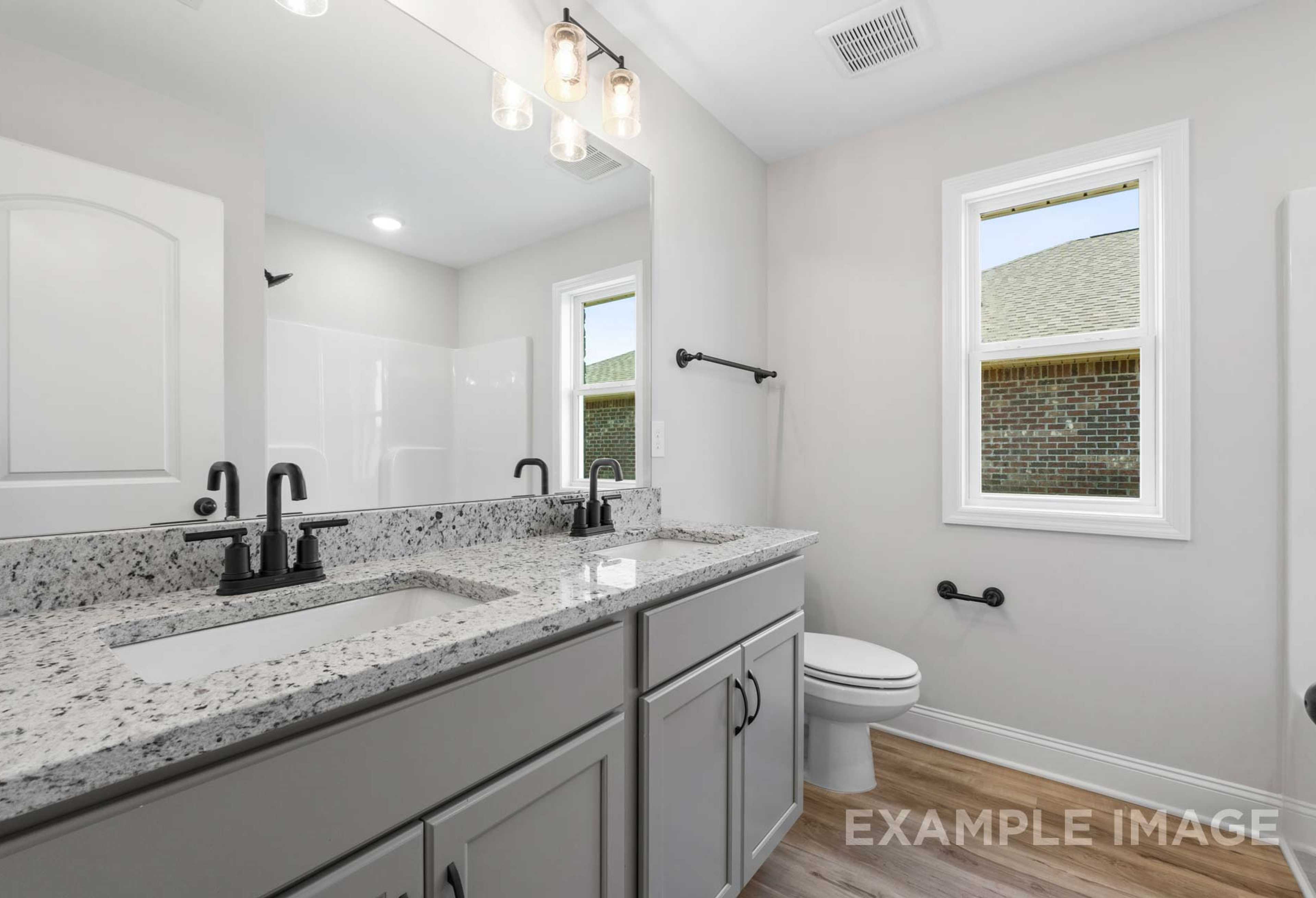 Modern master bathroom in The Holly M featuring double gray vanity, quartz counters, black faucets, and pendant lights