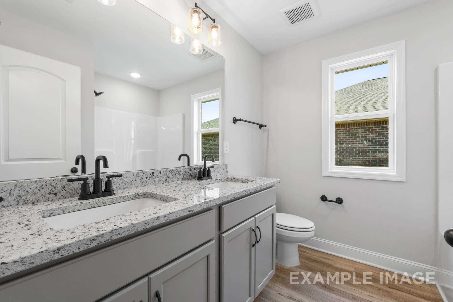 Modern master bathroom in The Holly M featuring double gray vanity, quartz counters, black faucets, and pendant lights