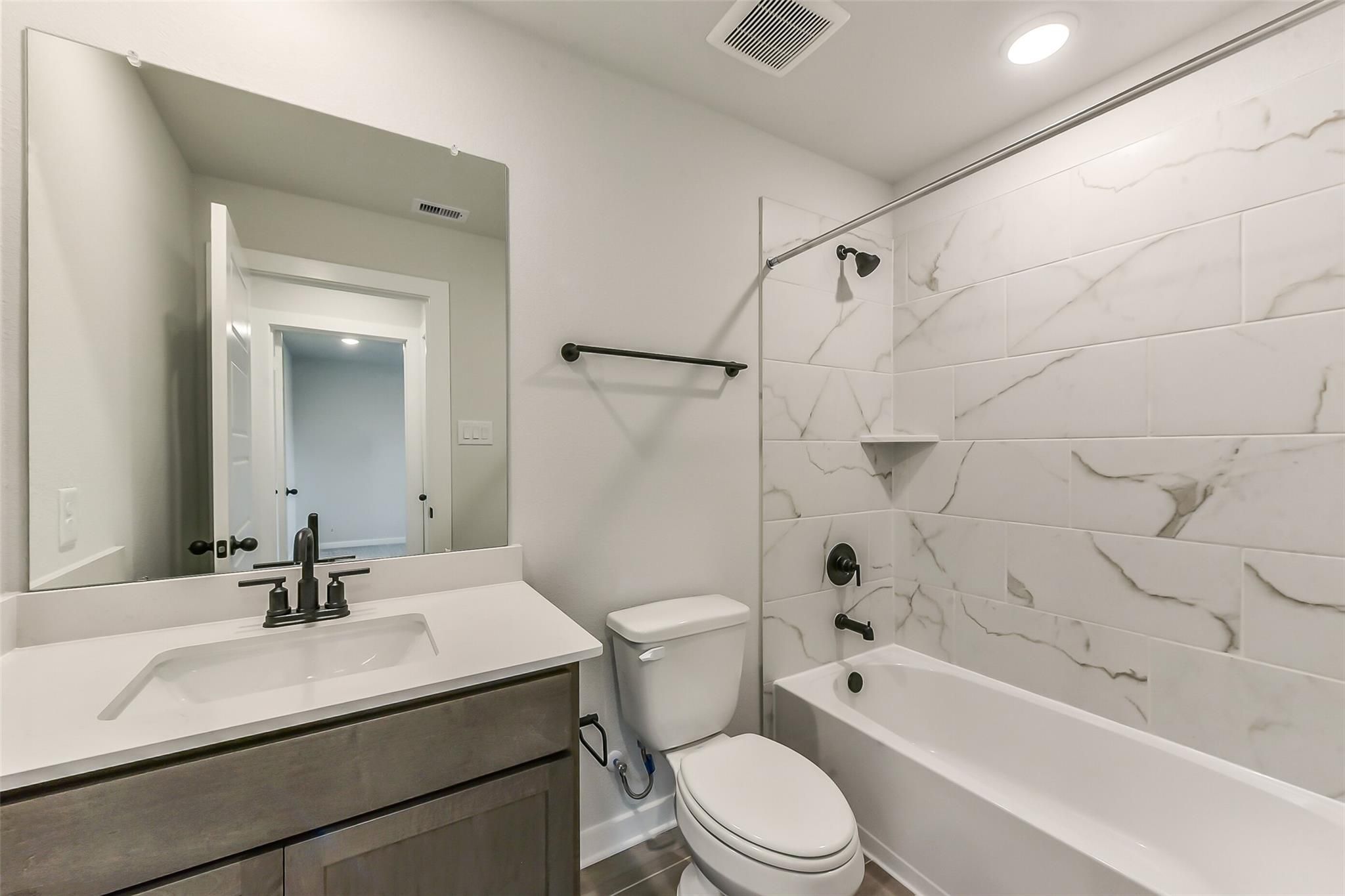 Elegant bathroom with marble-look subway tiles, tub-shower combo, gray vanity, and black fixtures in Davidson Homes Sequoia C, Crosby TX