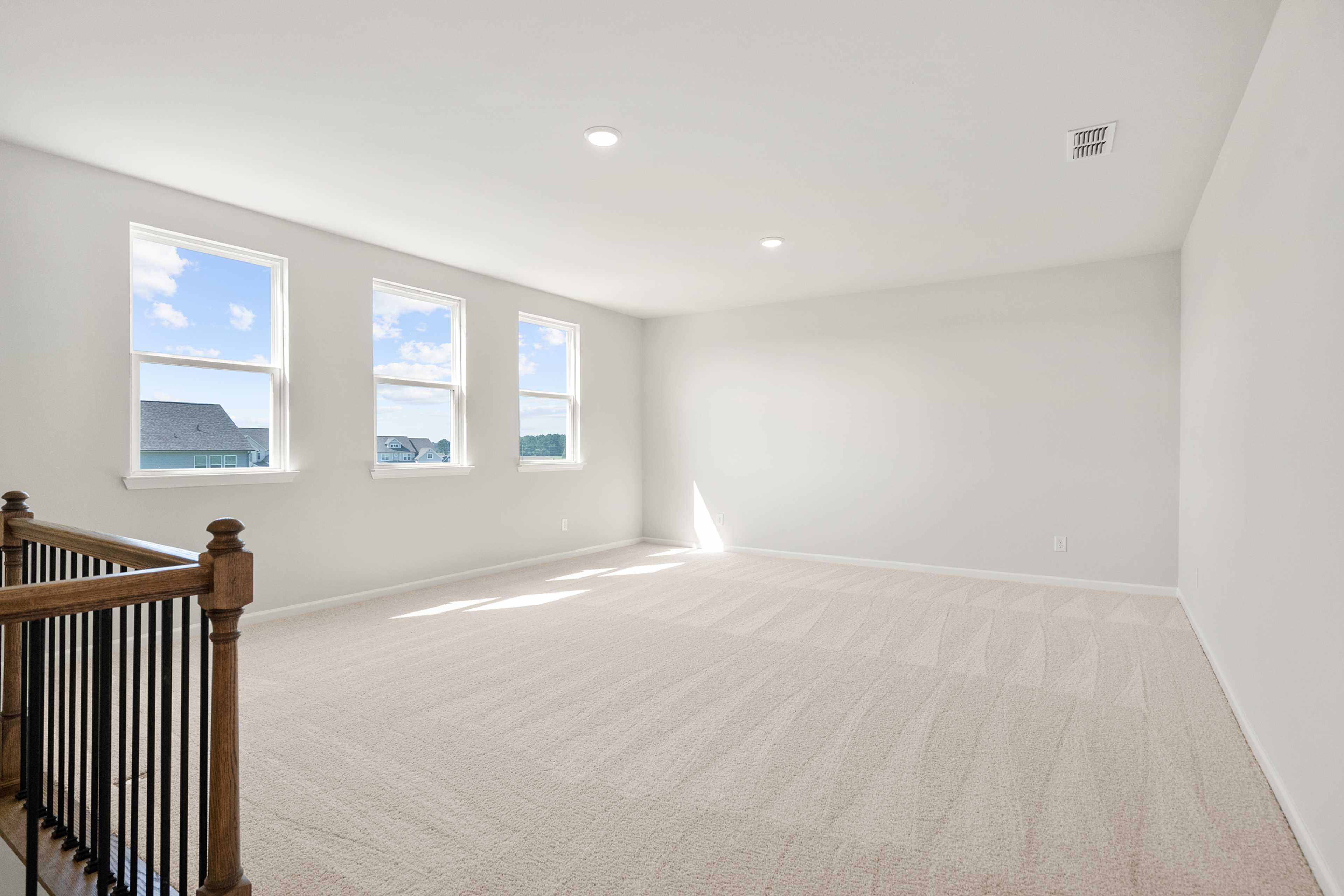 Spacious bonus room at The Everleigh in Locust Grove GA with beige carpet, large windows and wooden staircase