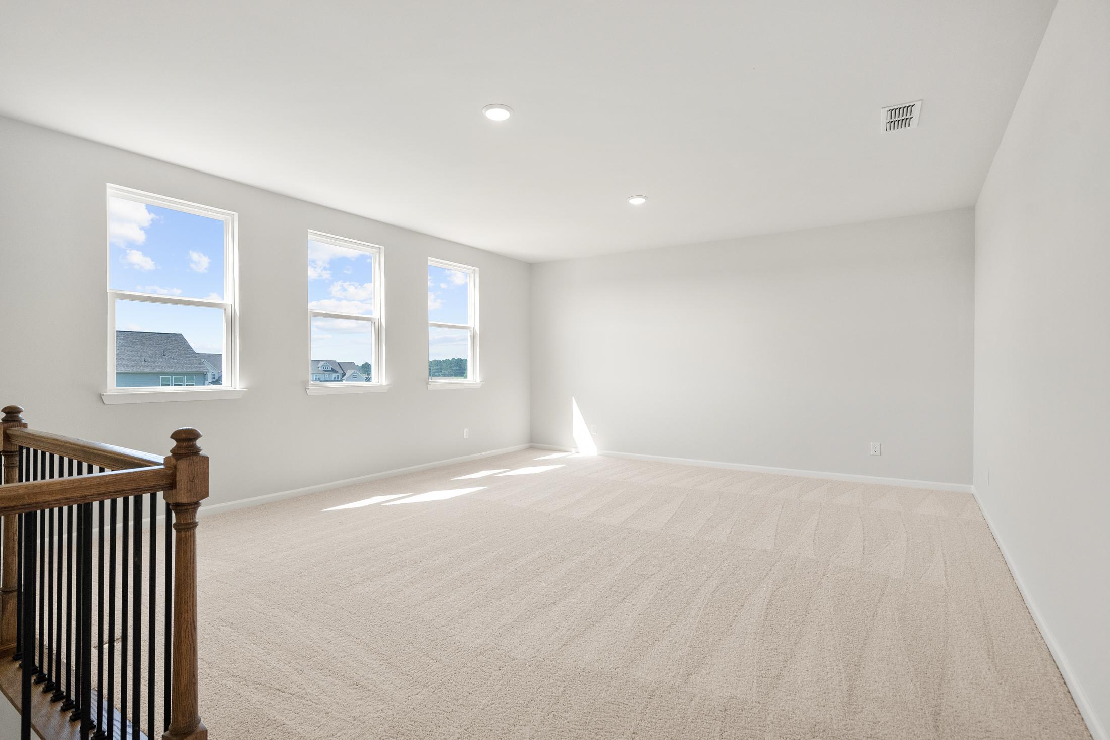 Spacious bonus room at The Everleigh in Locust Grove GA with beige carpet, large windows and wooden staircase