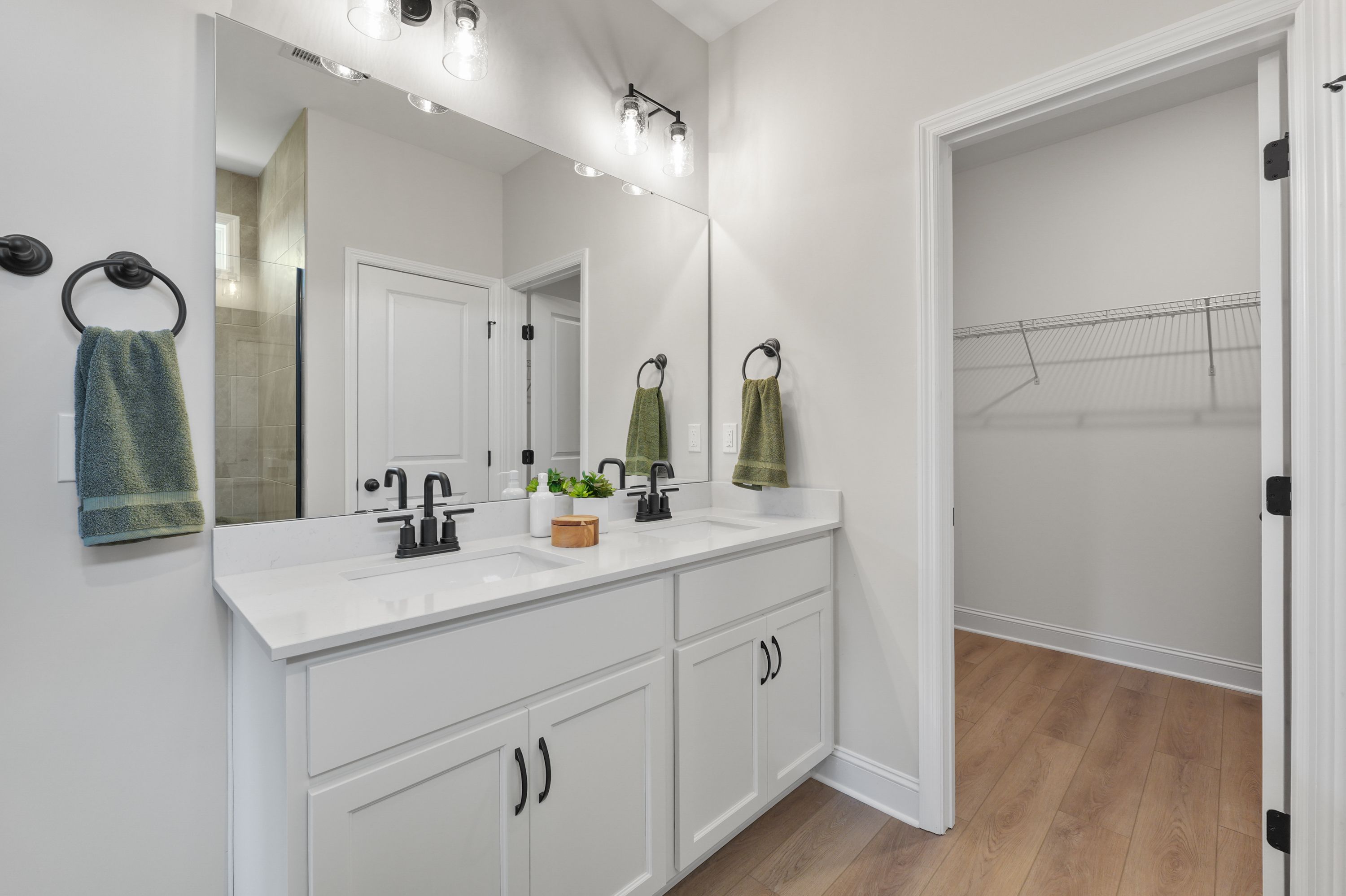 Modern double vanity bathroom at Ramsay Cove in Owens Cross Roads, Alabama with mirrors, green towels, plant, and walk-in closet