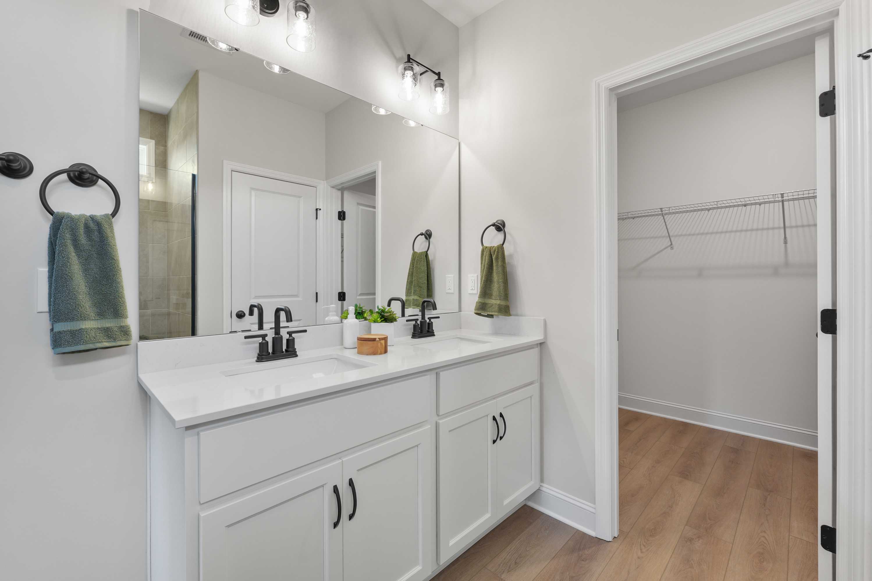Modern double vanity bathroom at Ramsay Cove in Owens Cross Roads, Alabama with mirrors, green towels, plant, and walk-in closet