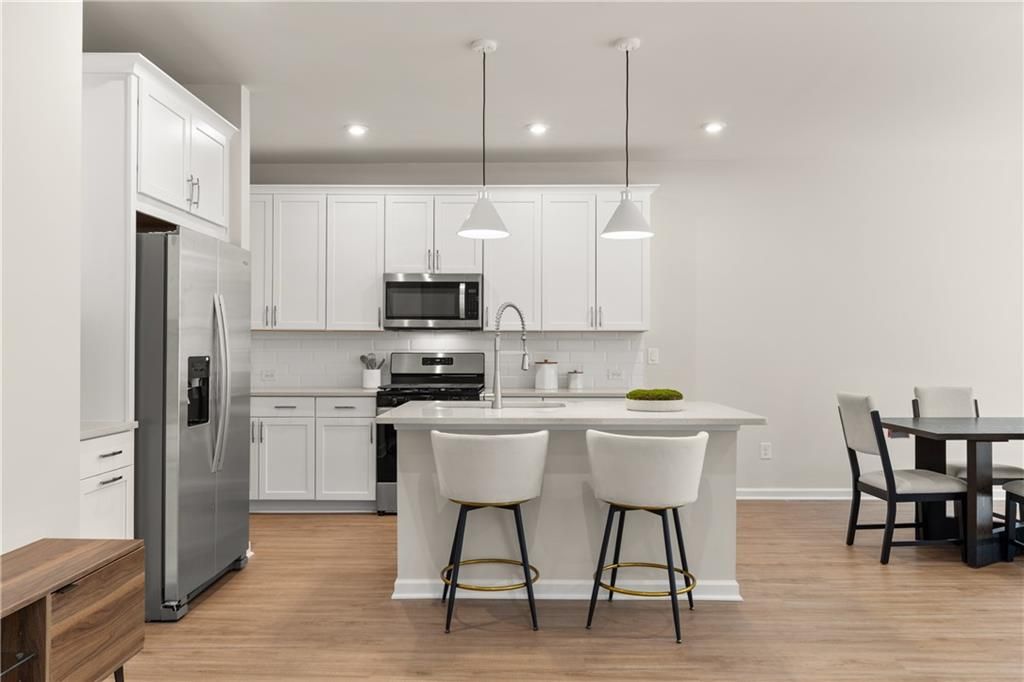 Modern white kitchen with stainless appliances, peninsula island, bar stools, and adjacent dining nook in Davidson Homes The Marion B, Kennesaw, Georgia