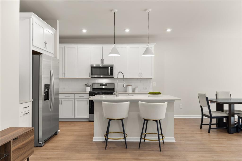 Modern white kitchen with stainless appliances, peninsula island, bar stools, and adjacent dining nook in Davidson Homes The Marion B, Kennesaw, Georgia