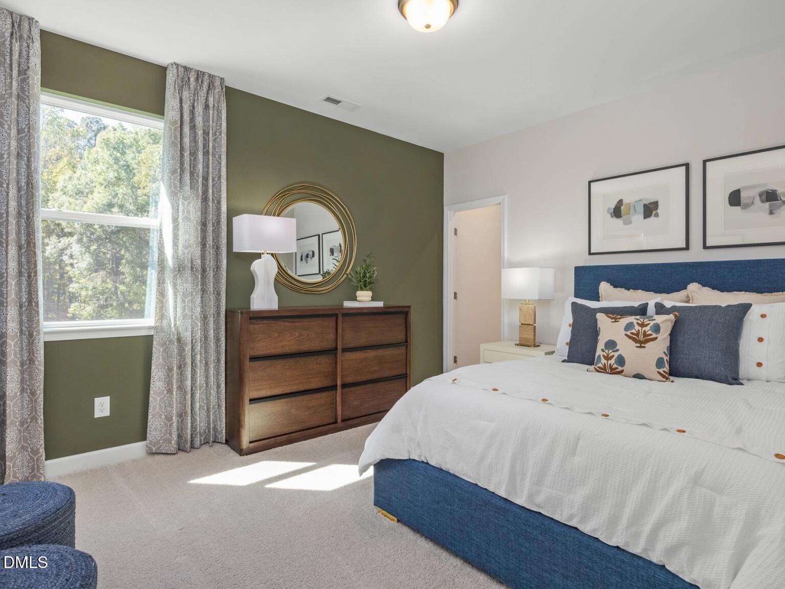 Elegant master bedroom with green accent wall, wooden dresser, blue upholstered bed, and large window in Davidson Homes The Hickory II D, Wake Forest, NC