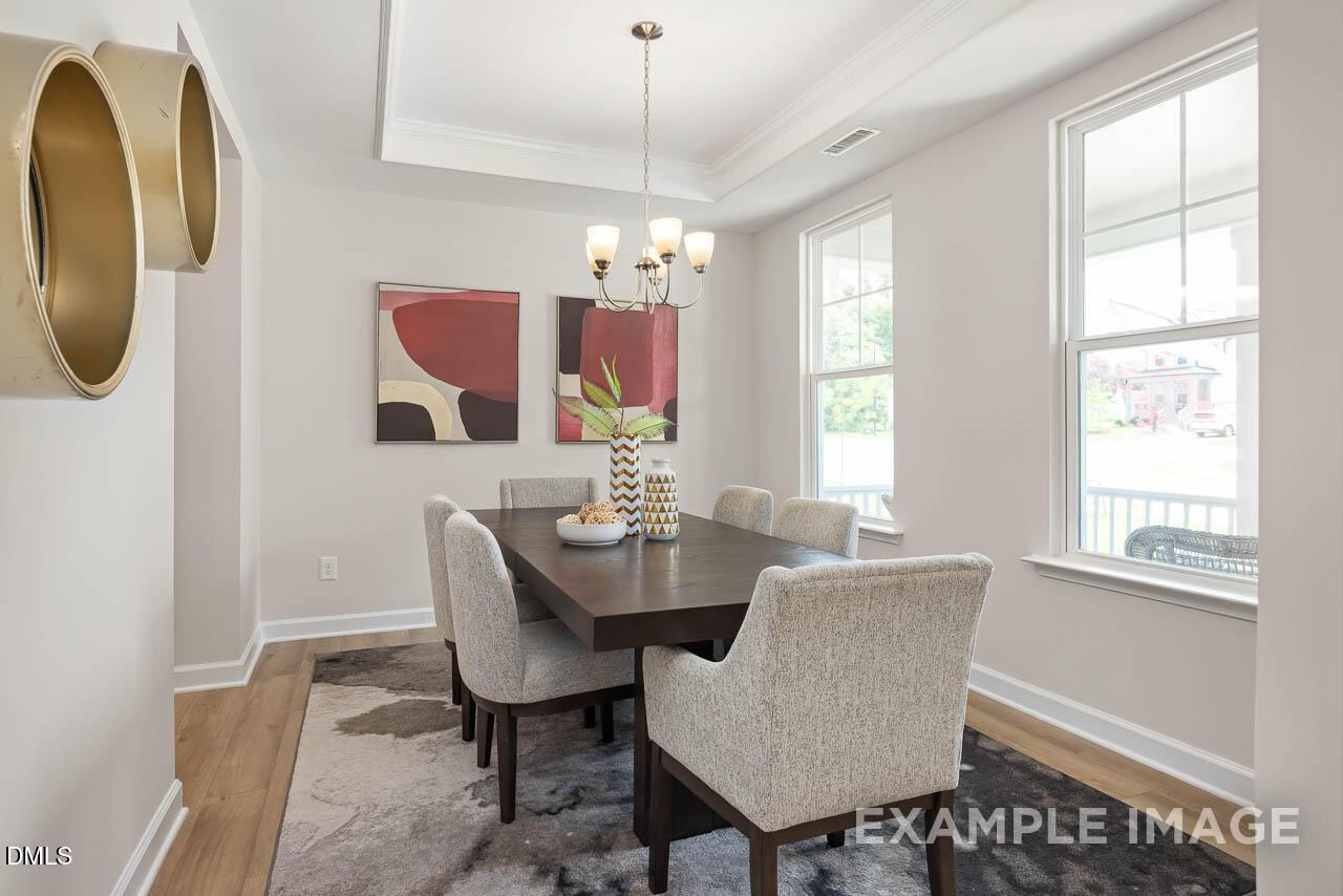 Elegant dining room featuring rectangular wood table, gray upholstered chairs, modern chandelier, abstract art, and backyard views in The Willow D, Lillington, NC