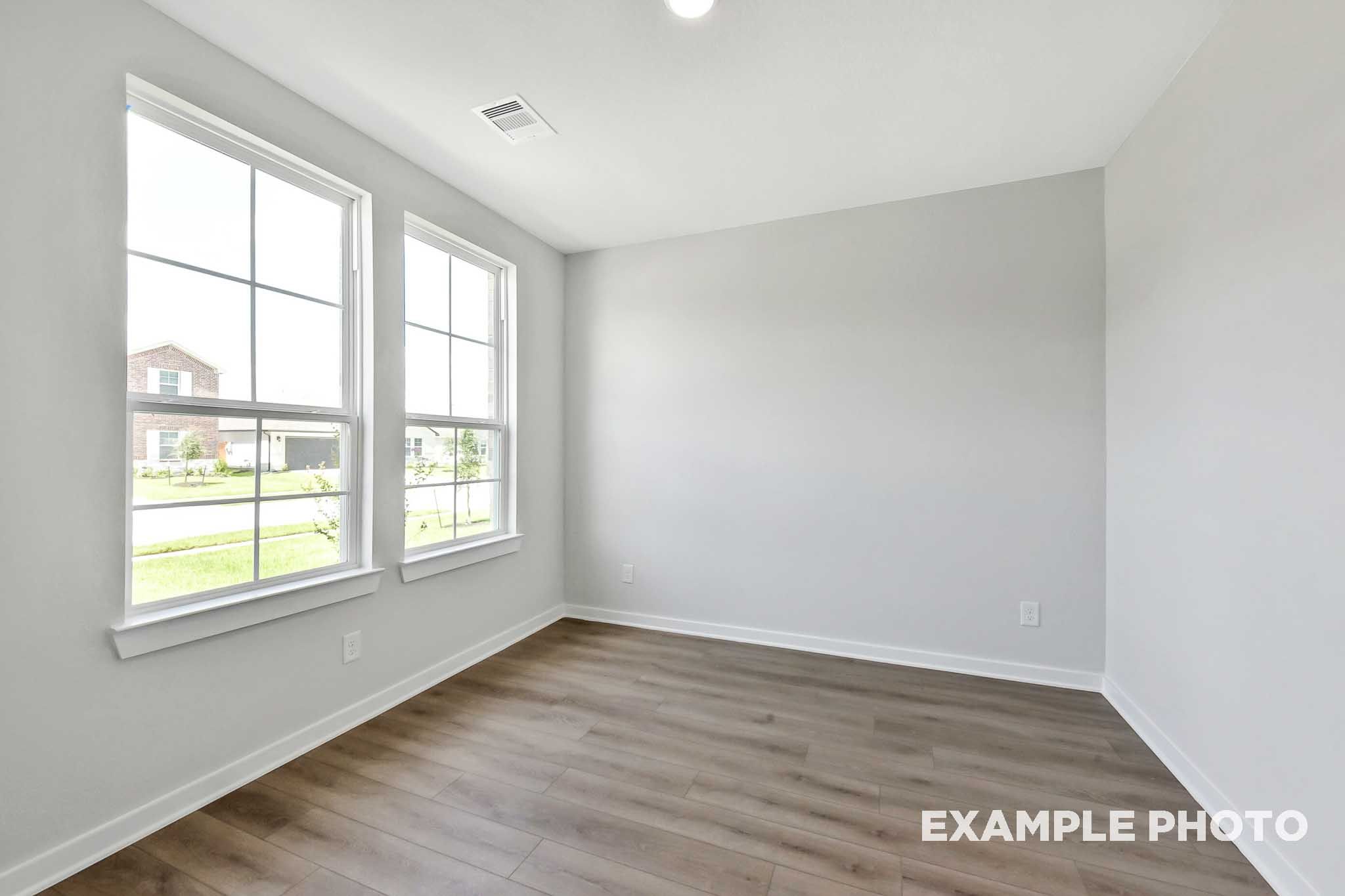 Spacious bedroom in The Sequoia home with large windows, gray walls, hardwood floors, and green lawn view