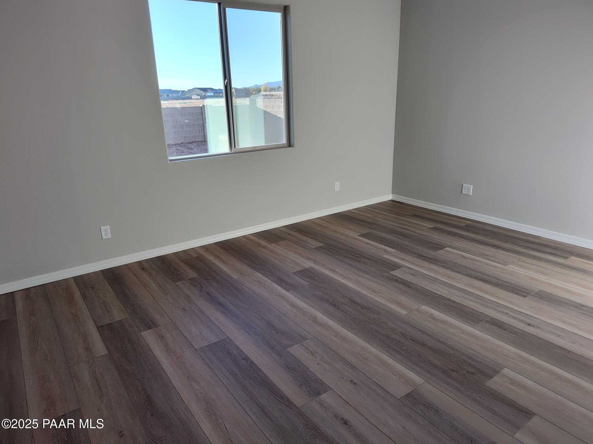Bright empty bedroom with large sunny window and wood-look flooring in Davidson Homes The Frontier C, Prescott Valley, AZ
