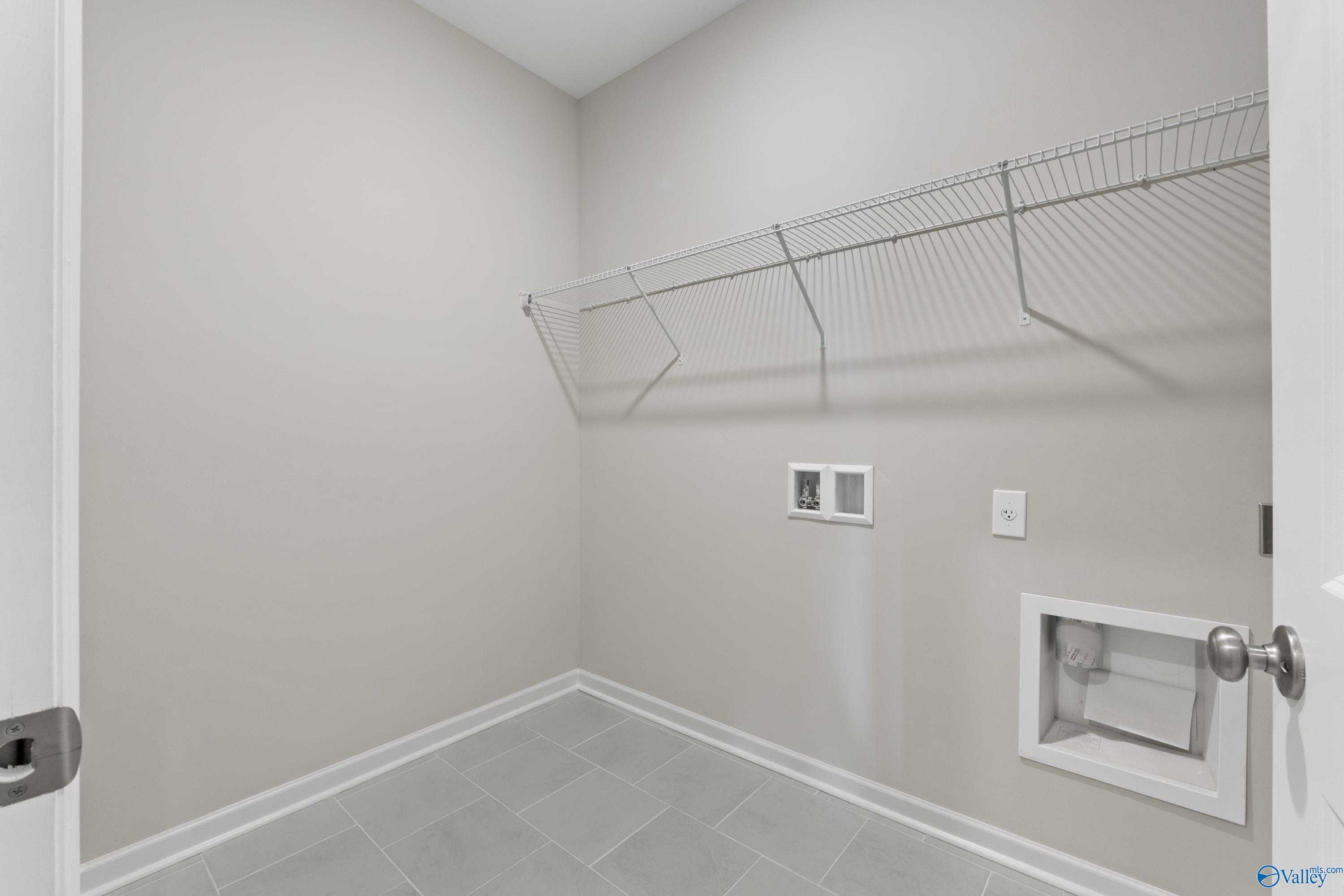 Spacious laundry room with wire shelving, utility sink, and washer-dryer hookups in Davidson Homes The Luna, Hazel Green, Alabama