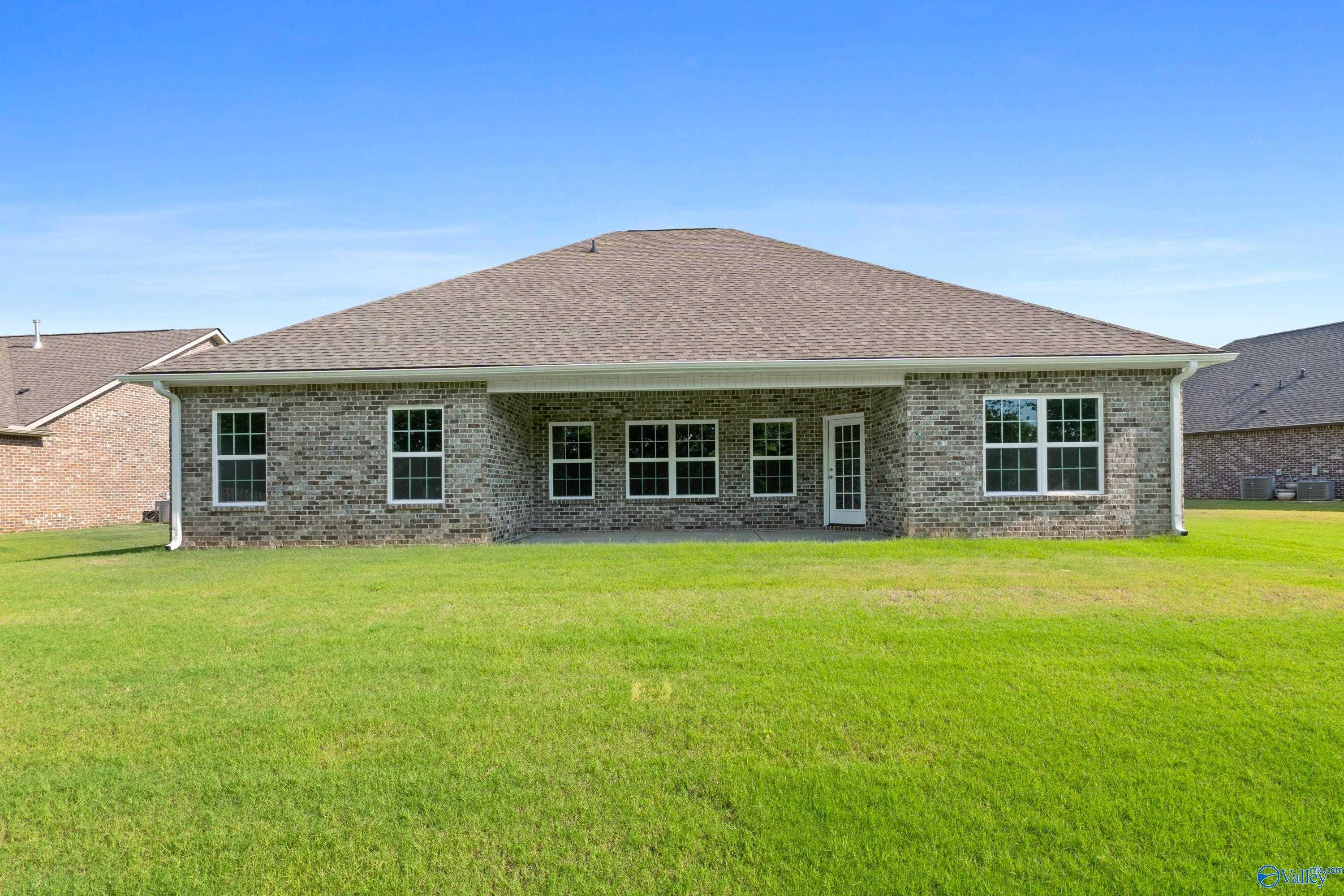Single-story brick home with covered back patio, large windows, and lush green backyard in Creekside, Harvest, Alabama - Davidson Homes The Rockford