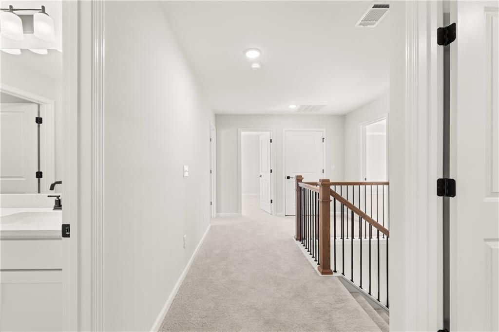 Upstairs hallway with white walls, carpeted floors, bathroom vanity, and wrought-iron staircase in Davidson Homes The Hickory B, Winder, GA