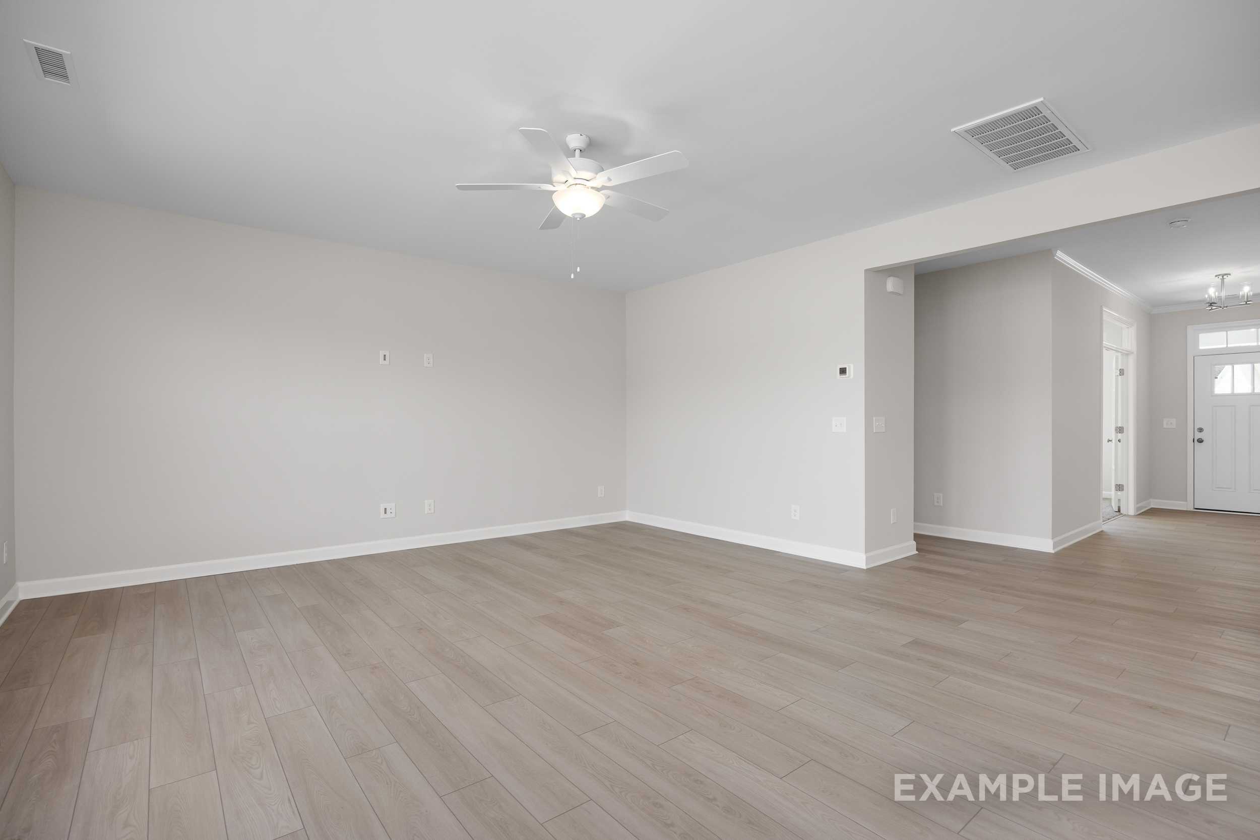 Spacious empty living area in The Hickory II home with neutral beige walls, ceiling fan, open doorway, and light hardwood floors