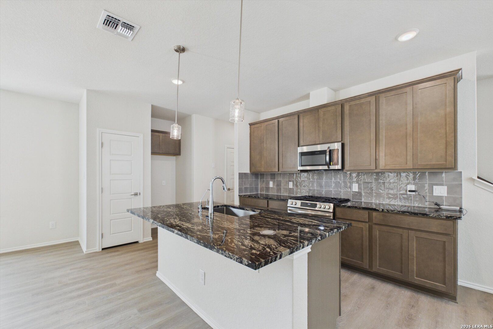 Modern kitchen with granite island and dark wood cabinets in The Charlotte B floor plan at Meadows at Oak Creek, San Antonio.