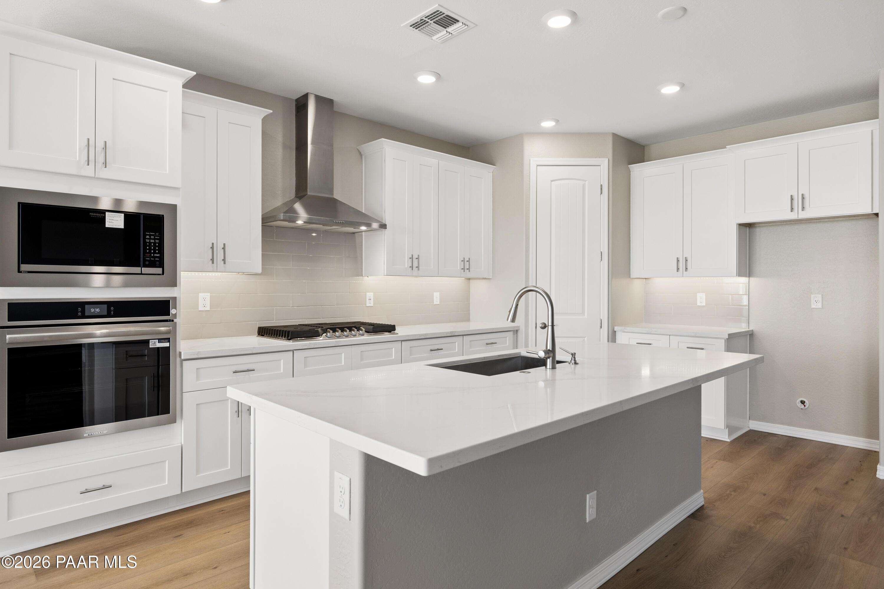 Modern white kitchen with stainless steel appliances, quartz island, and recessed lighting in Davidson Homes The Harmony A, Prescott Valley