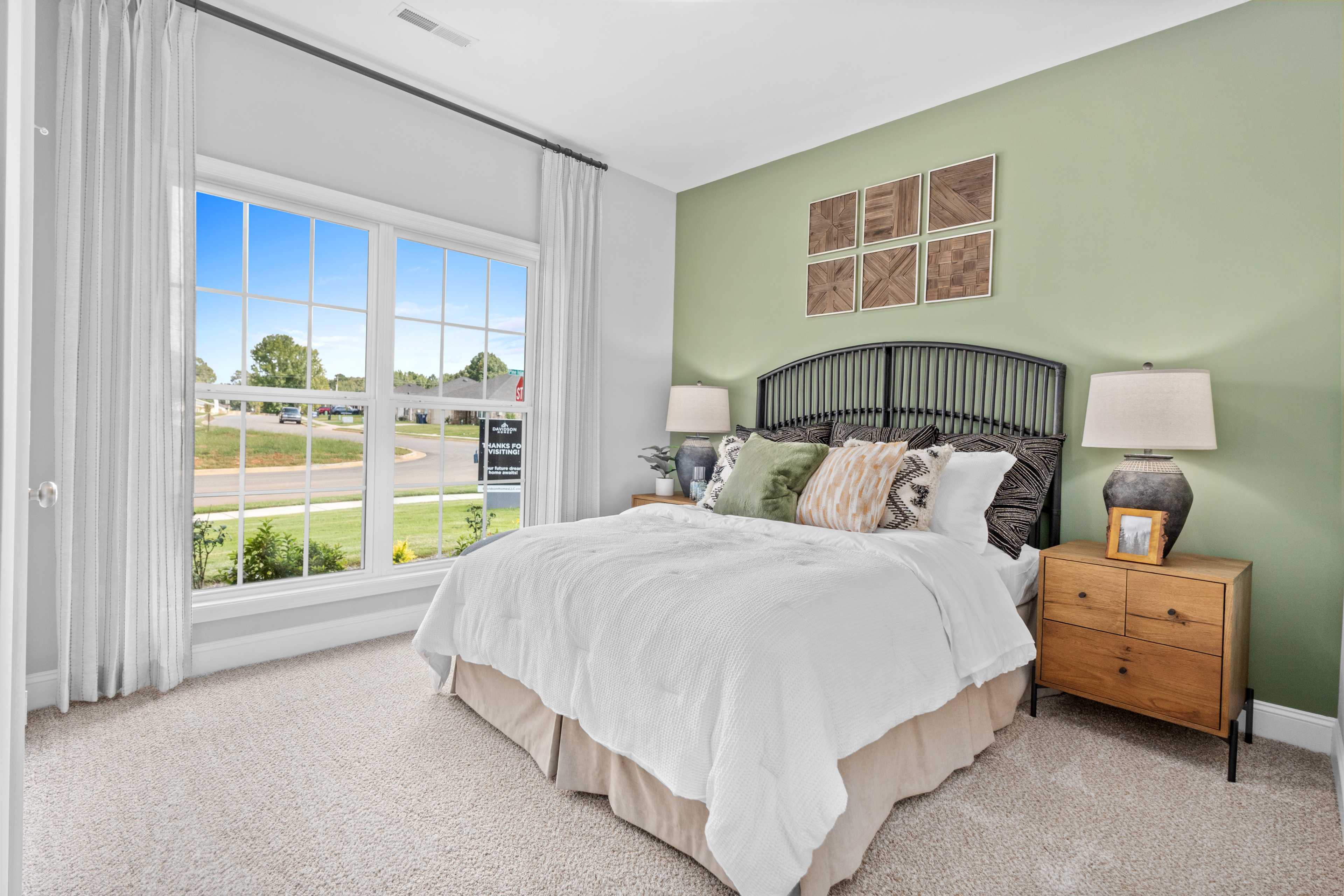 Spacious master bedroom at Wood Trail in Toney Alabama with large window, green accent wall, king bed, wrought iron headboard