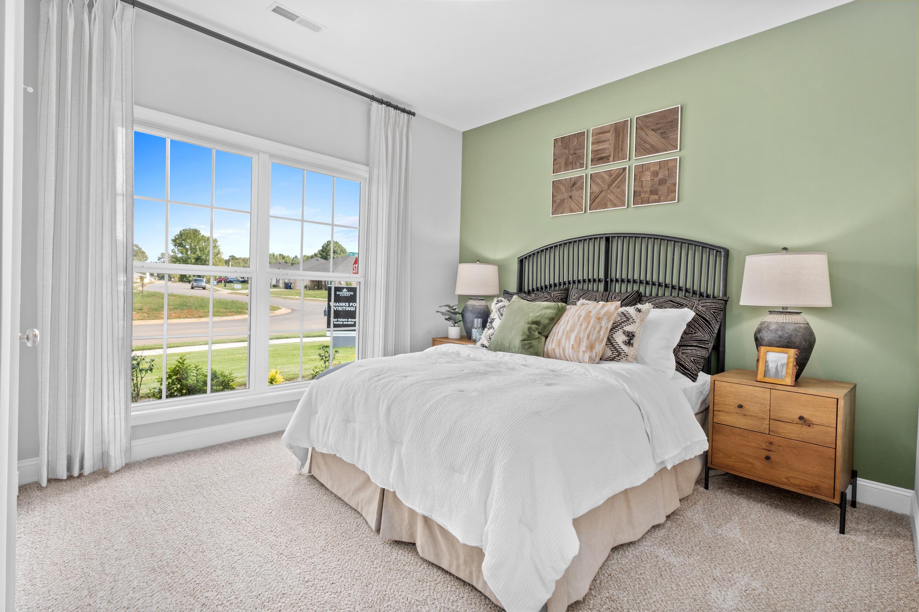 Spacious master bedroom at Wood Trail in Toney Alabama with large window, green accent wall, king bed, wrought iron headboard