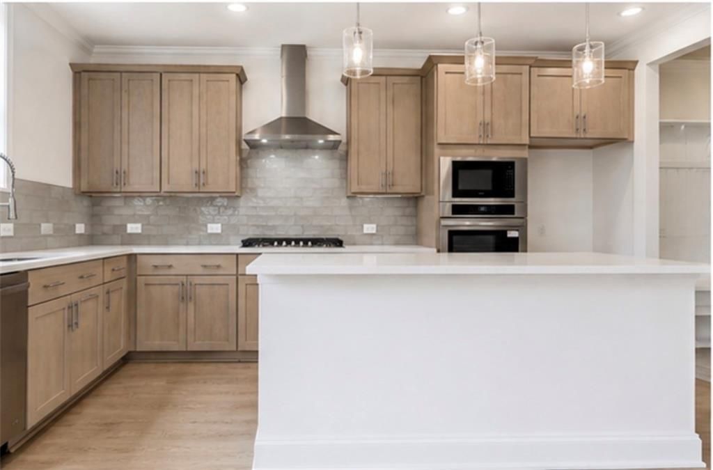 Modern kitchen with light wood cabinets, quartz island, and stainless appliances in The Hickory C home, Wehunt Meadows.