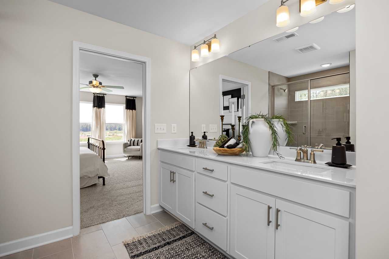 Spacious master bathroom at Wellers Knoll in Lillington NC with double vanity, greenery accents and open bedroom view