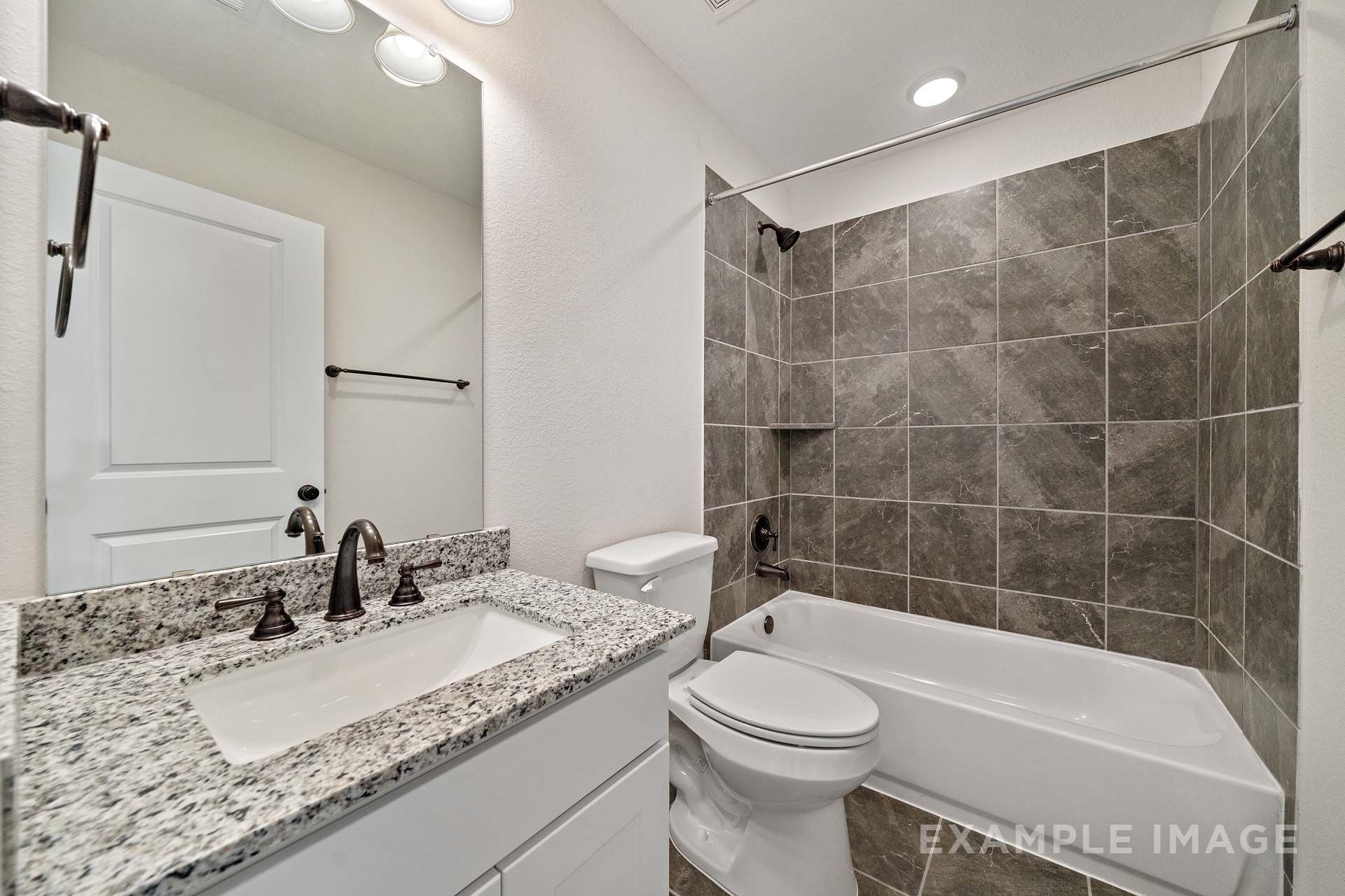 Bathroom in The Victoria by Davidson Homes featuring granite vanity, oil-rubbed bronze fixtures, and gray tile tub shower