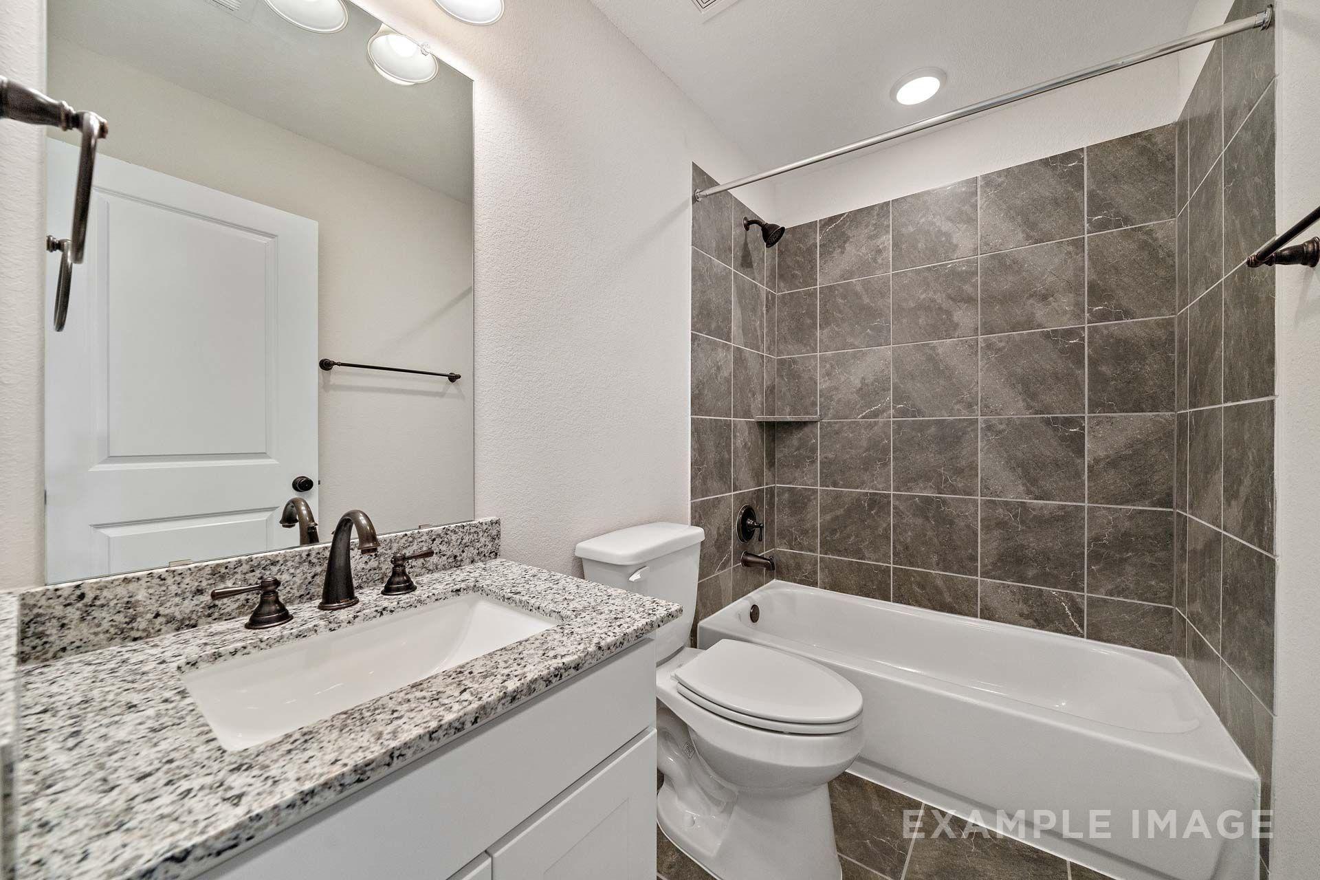 Bathroom in The Victoria by Davidson Homes featuring granite vanity, oil-rubbed bronze fixtures, and gray tile tub shower
