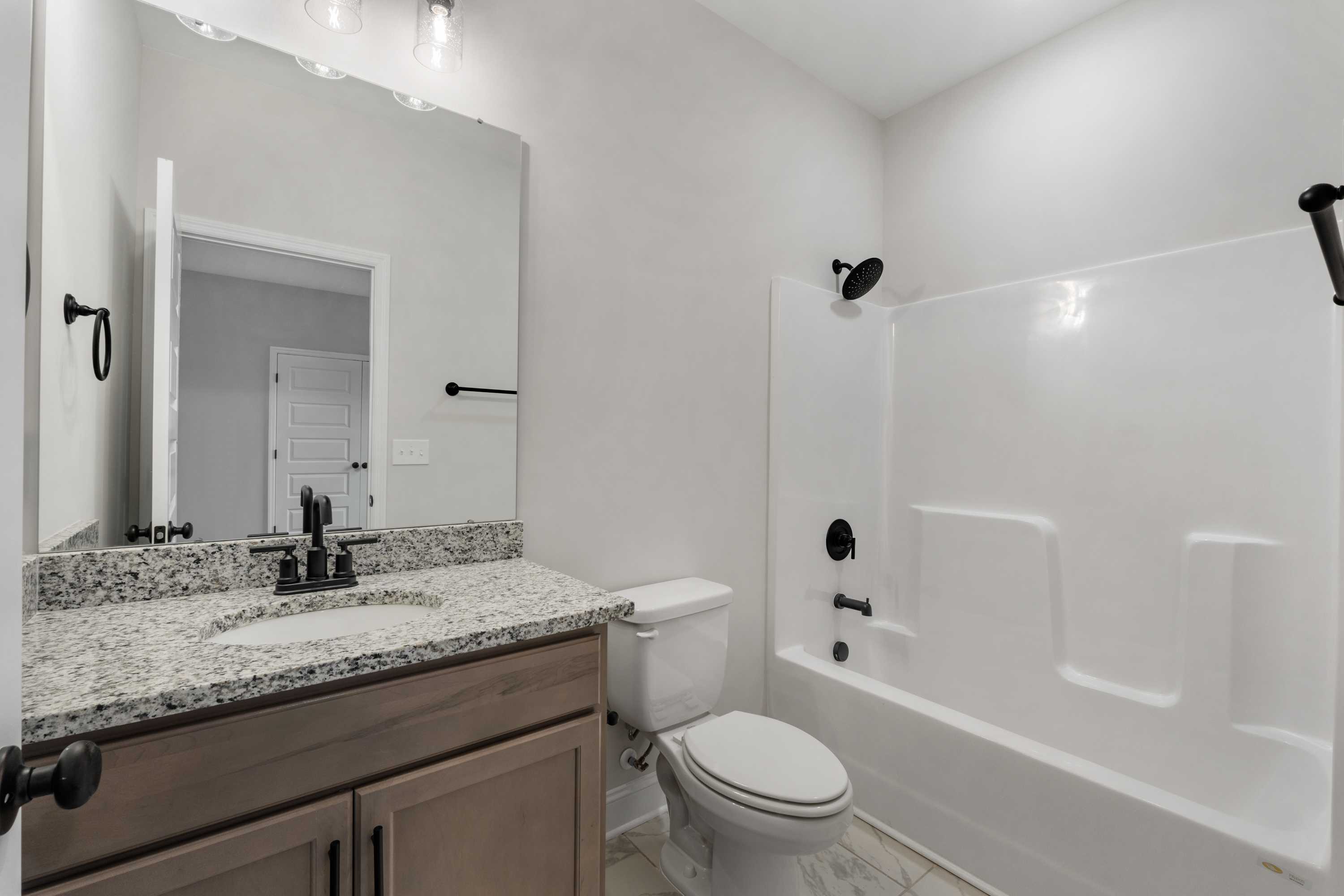 Master bathroom in The Oxford by Davidson Homes featuring granite vanity, white tub-shower combo, and modern fixtures