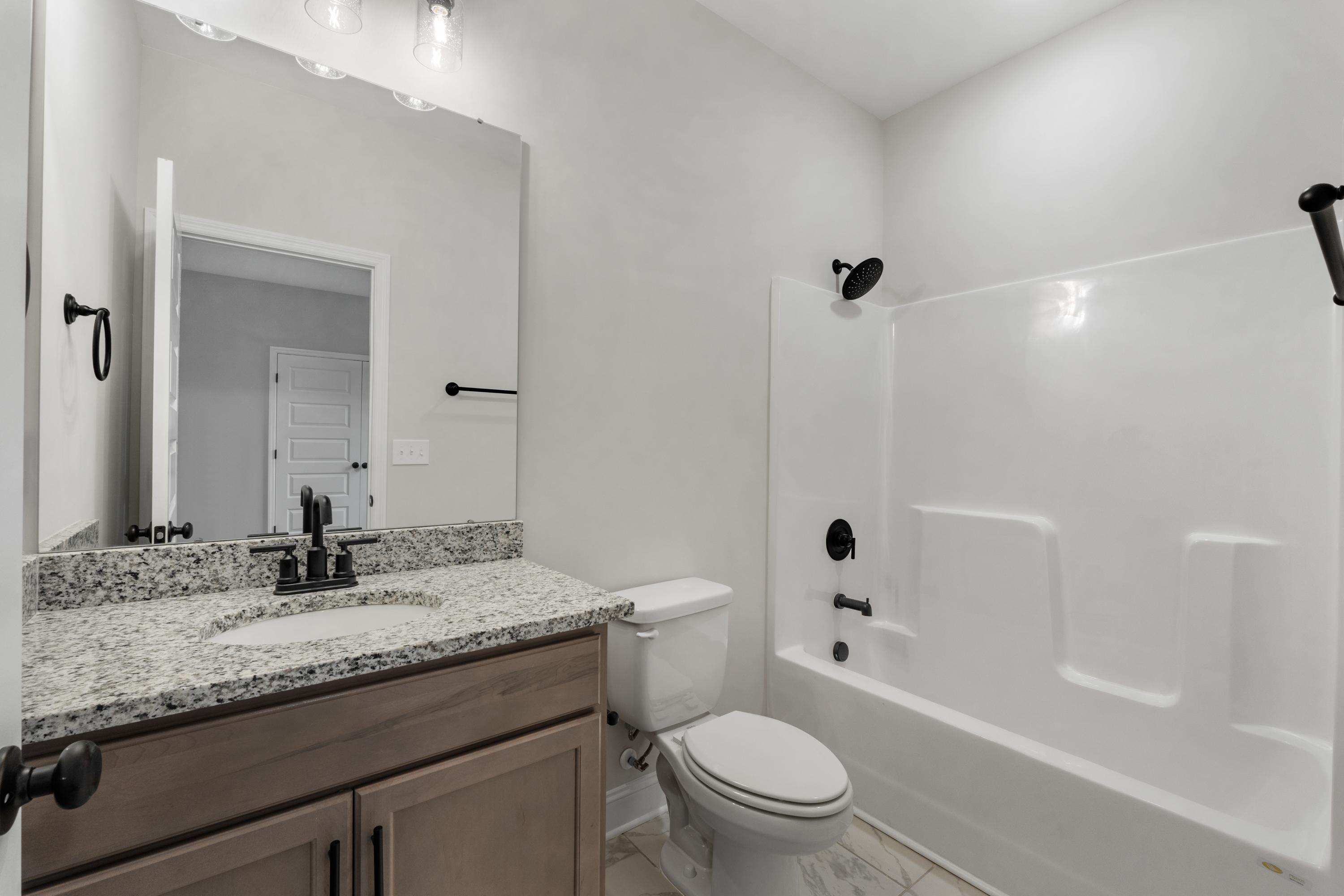 Master bathroom in The Oxford by Davidson Homes featuring granite vanity, white tub-shower combo, and modern fixtures