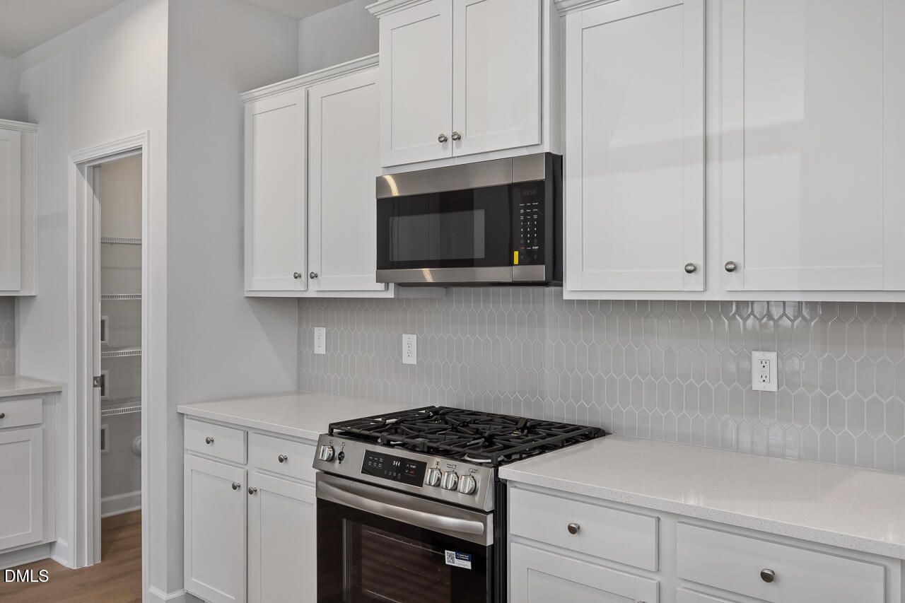 Modern kitchen with white cabinets, stainless steel appliances, and tile backsplash in The Adalynn B, Gregory Village home.