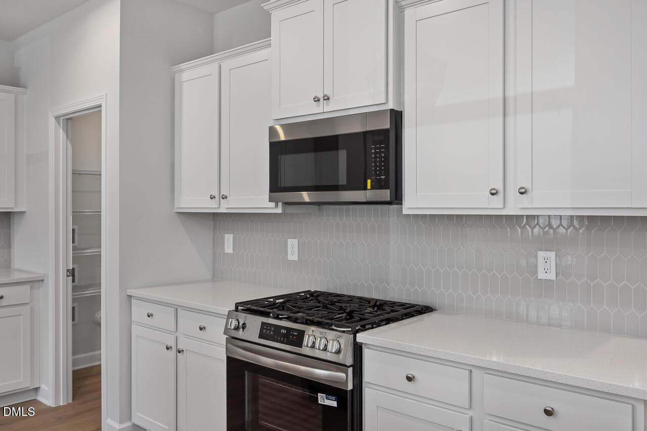Modern kitchen with white shaker cabinets, gas range, and gray picket tile backsplash in Davidson Homes Adalynn B floor plan.