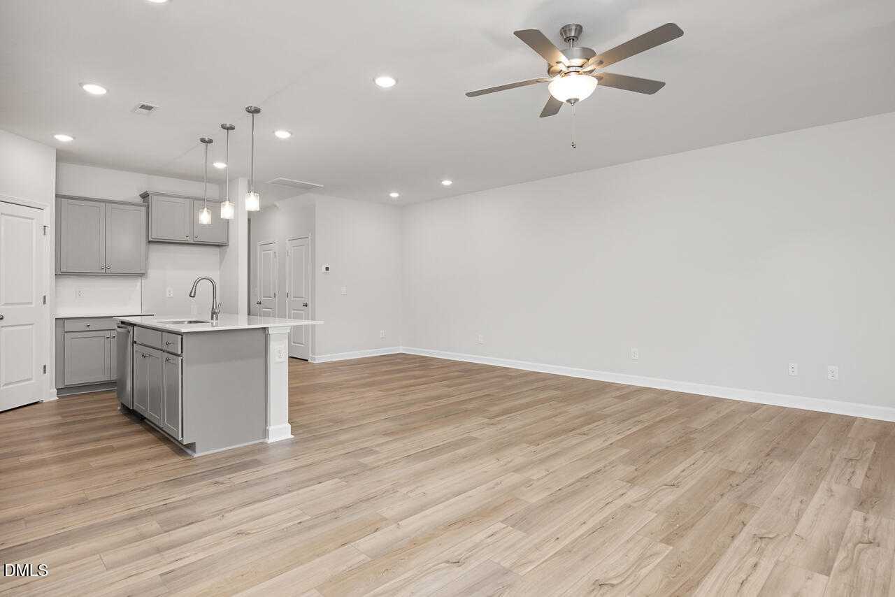 Modern open kitchen with gray island sink, pendant lights, ceiling fans, and hardwood floors in The Warren Davidson Homes, Fuquay-Varina, NC