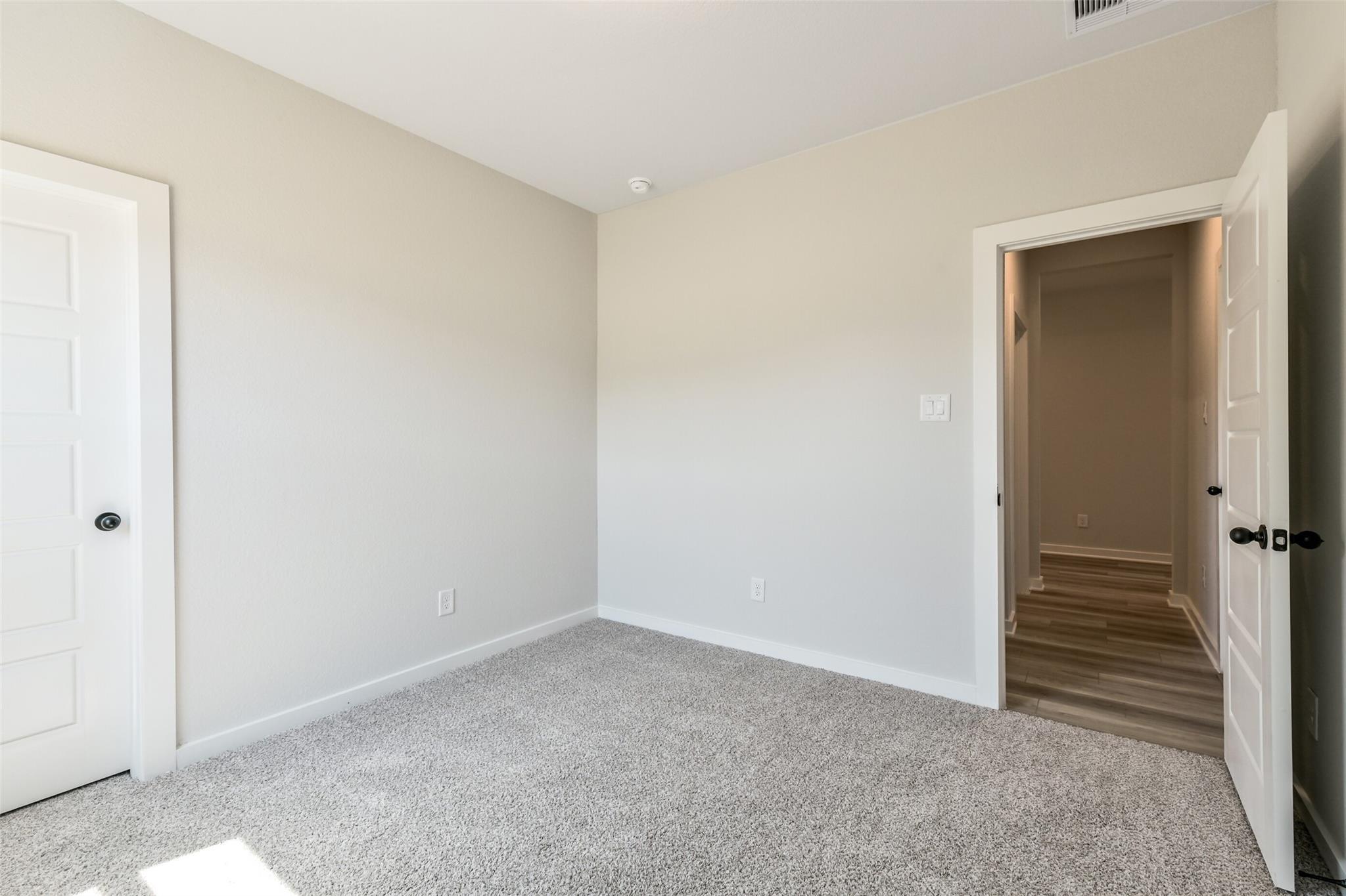 Spacious master bedroom with beige walls, carpeted floors, and en-suite access in Davidson Homes The Daphne H, Crosby, Texas