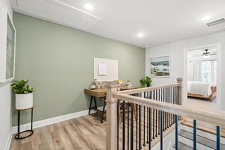 Upper floor loft office in The Washington H townhome with rustic wooden desk, potted plants, and sage green walls overlooking master suite stairs