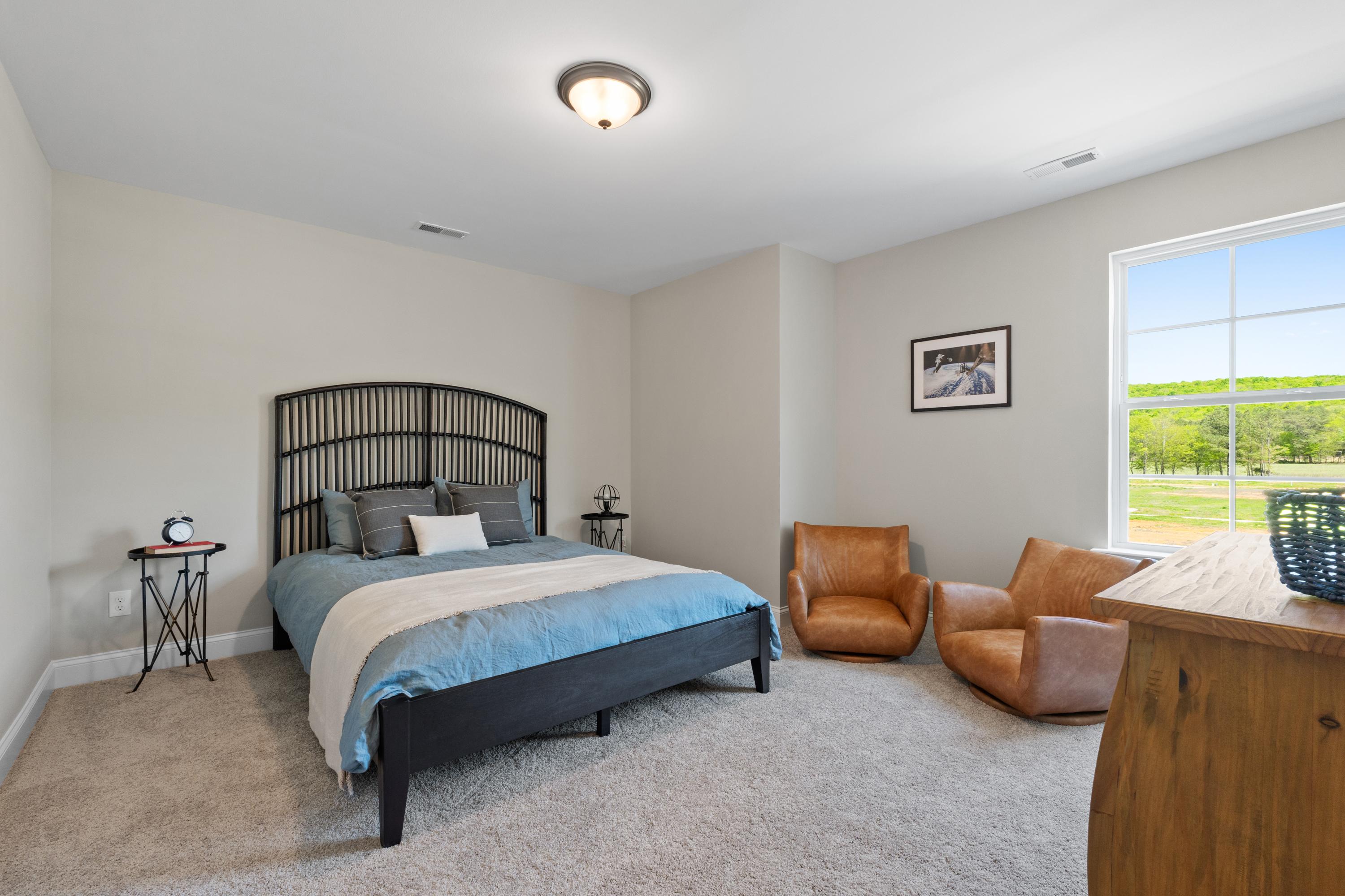 Spacious secondary bedroom in The Haven D by Evermore Homes featuring black iron bed, orange armchairs, and window view