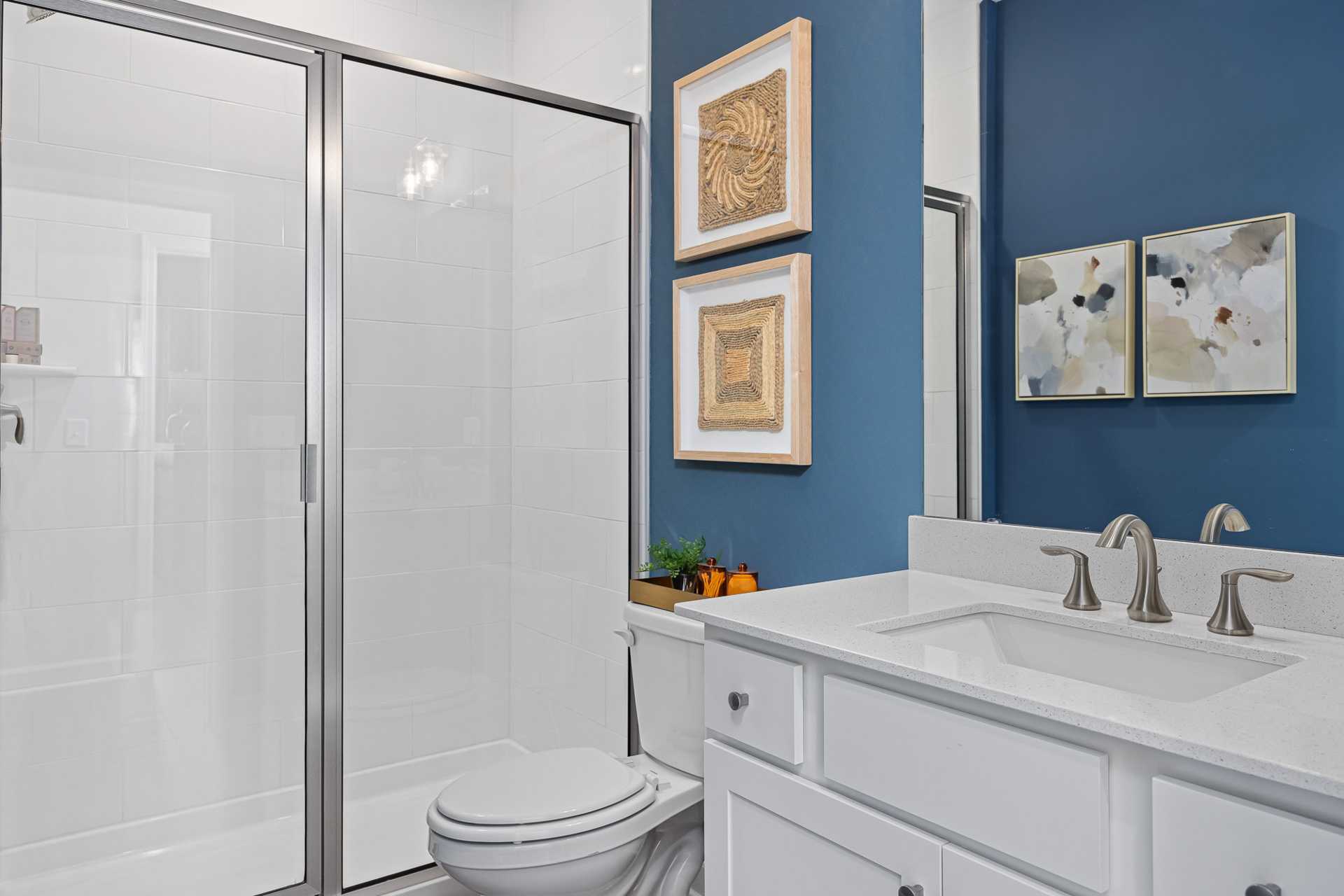 Modern bathroom in Beverly Place, Four Oaks NC with glass shower, navy accent wall, woven art, white vanity and fixtures by Davidson Homes