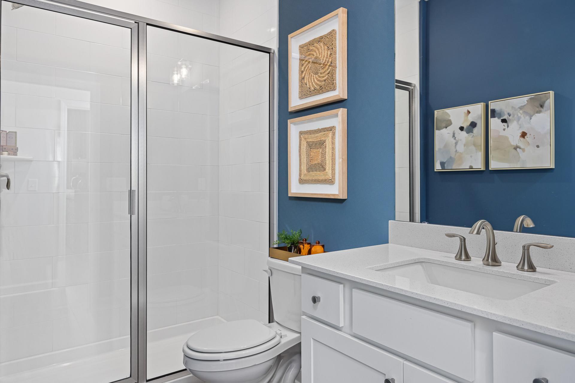 Modern bathroom in Beverly Place, Four Oaks NC with glass shower, navy accent wall, woven art, white vanity and fixtures by Davidson Homes