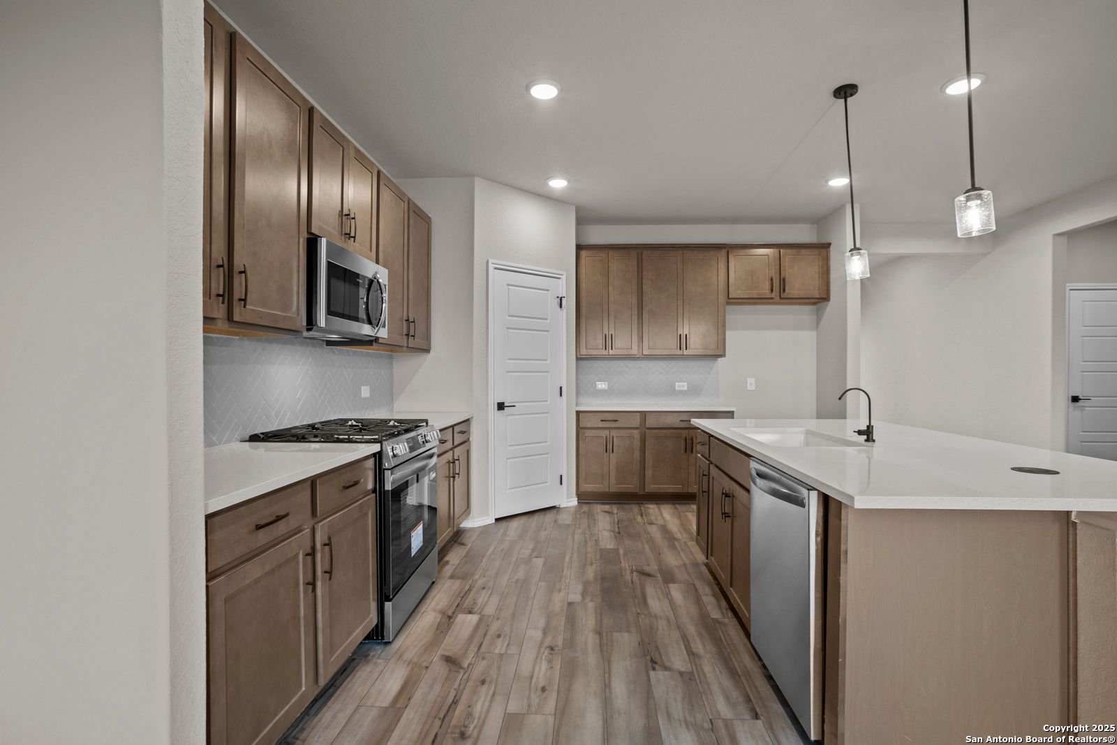 Modern kitchen with warm oak cabinets, stainless steel appliances, white quartz island, and subway tile backsplash in Davidson Homes The Douglas F, Comanche Ridge, San Antonio