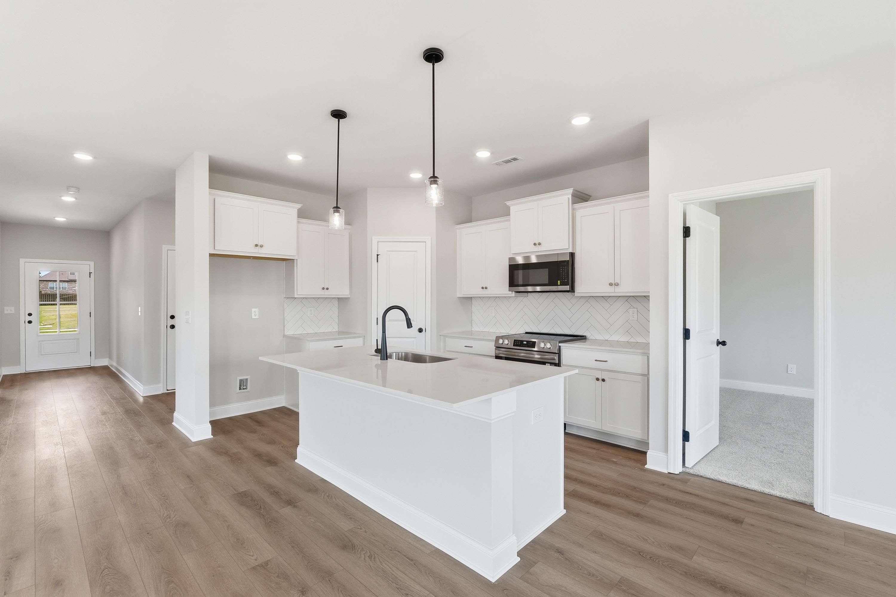 Modern kitchen in The Glen A featuring white cabinets, a large quartz island, and wood-style flooring in Josephine, Texas.