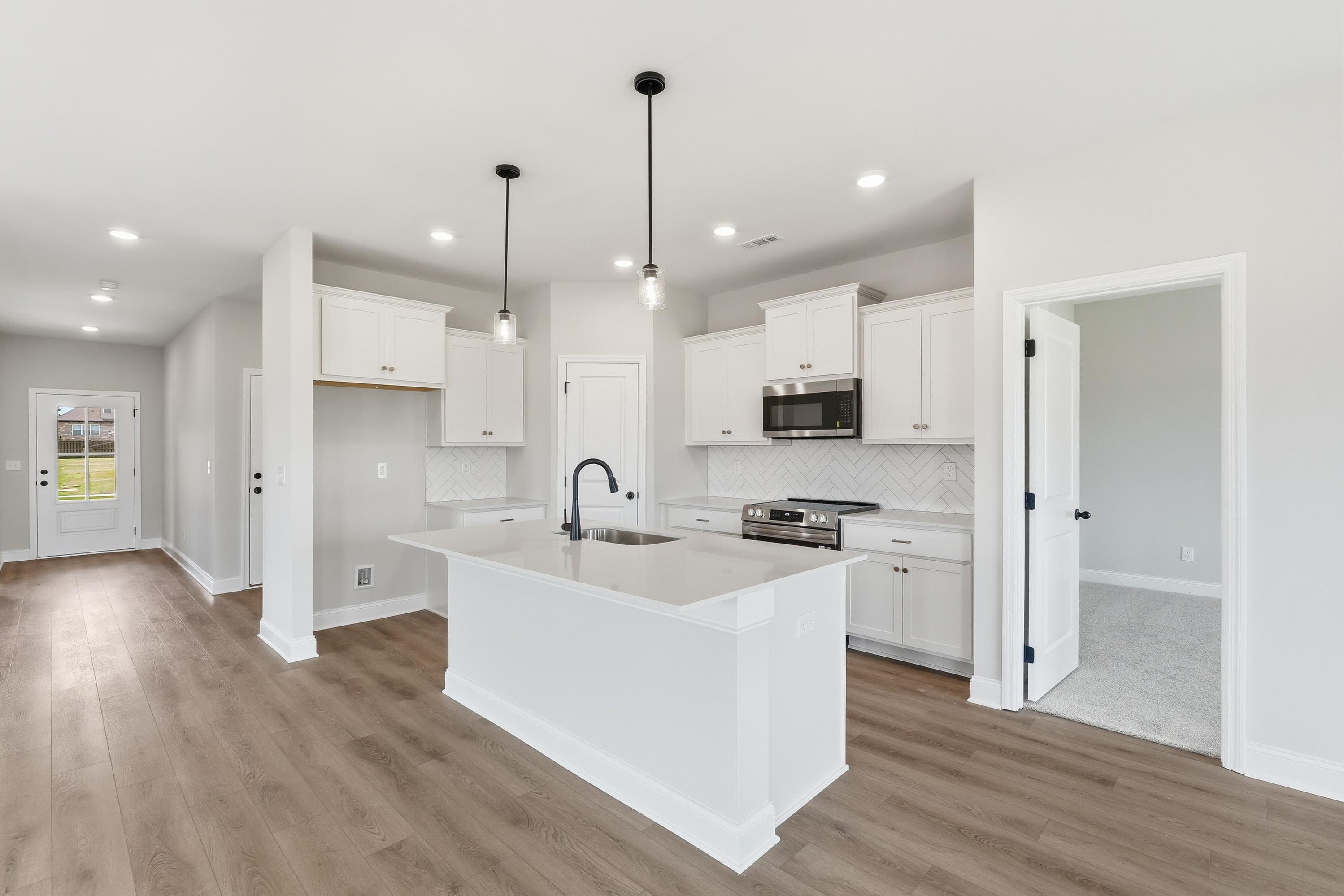 Modern kitchen in The Glen A featuring white cabinets, a large quartz island, and wood-style flooring in Josephine, Texas.