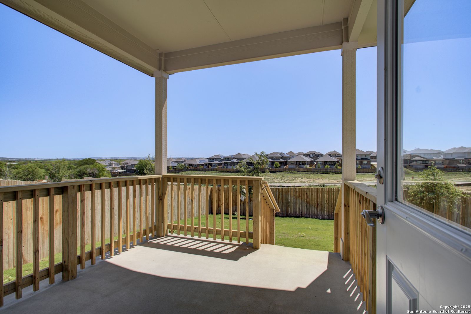 Covered back deck with wooden railing overlooking fenced grassy yard and Comanche Ridge neighborhood homes in San Antonio, Texas