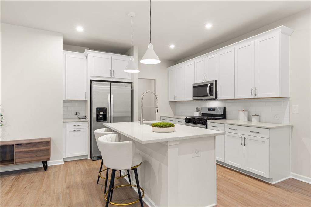 Modern white kitchen island with quartz counters, stainless steel appliances, and pendant lights in Davidson Homes The Marion B, Kennesaw, GA