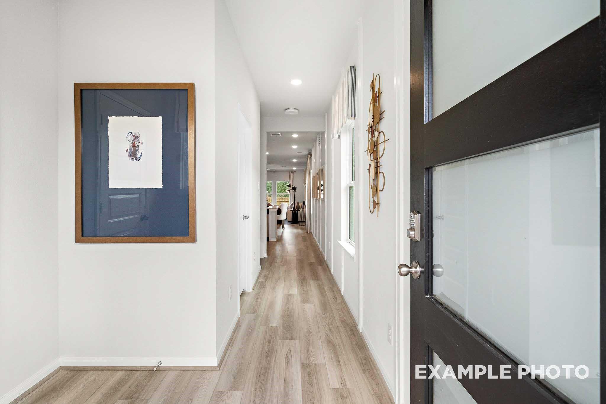 Bright hallway with hardwood floors, white walls, framed art, and frosted glass door in Davidson Homes San Marcos E, Conroe, Texas