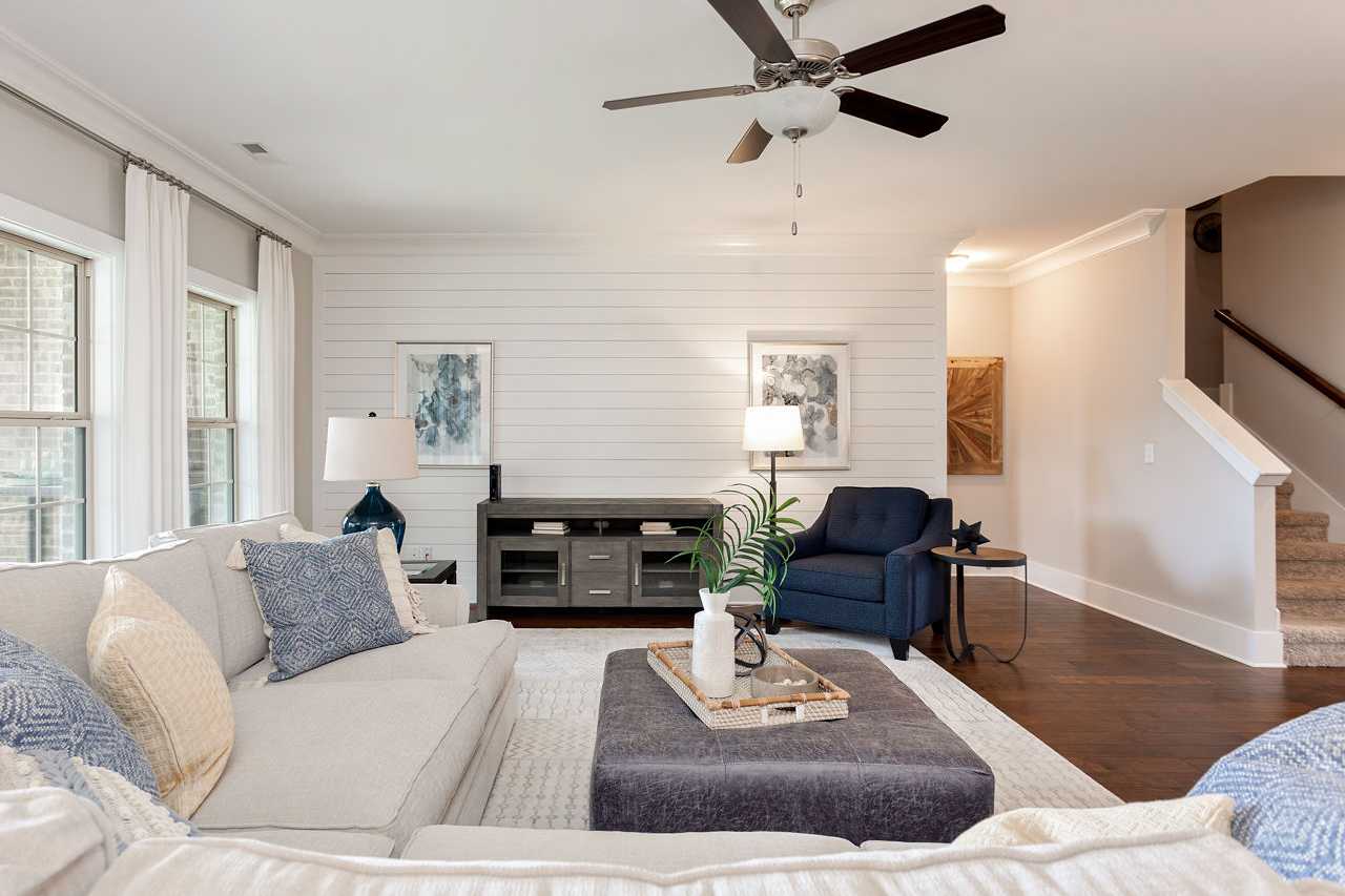 Spacious living room in The Rockford by Davidson Homes with cozy beige sectional, shiplap wall, ceiling fan, and open staircase